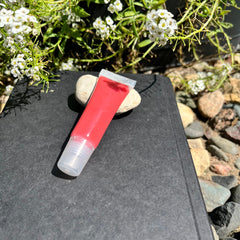 Rose lip gloss, red tube with clear applicator, resting on a rock