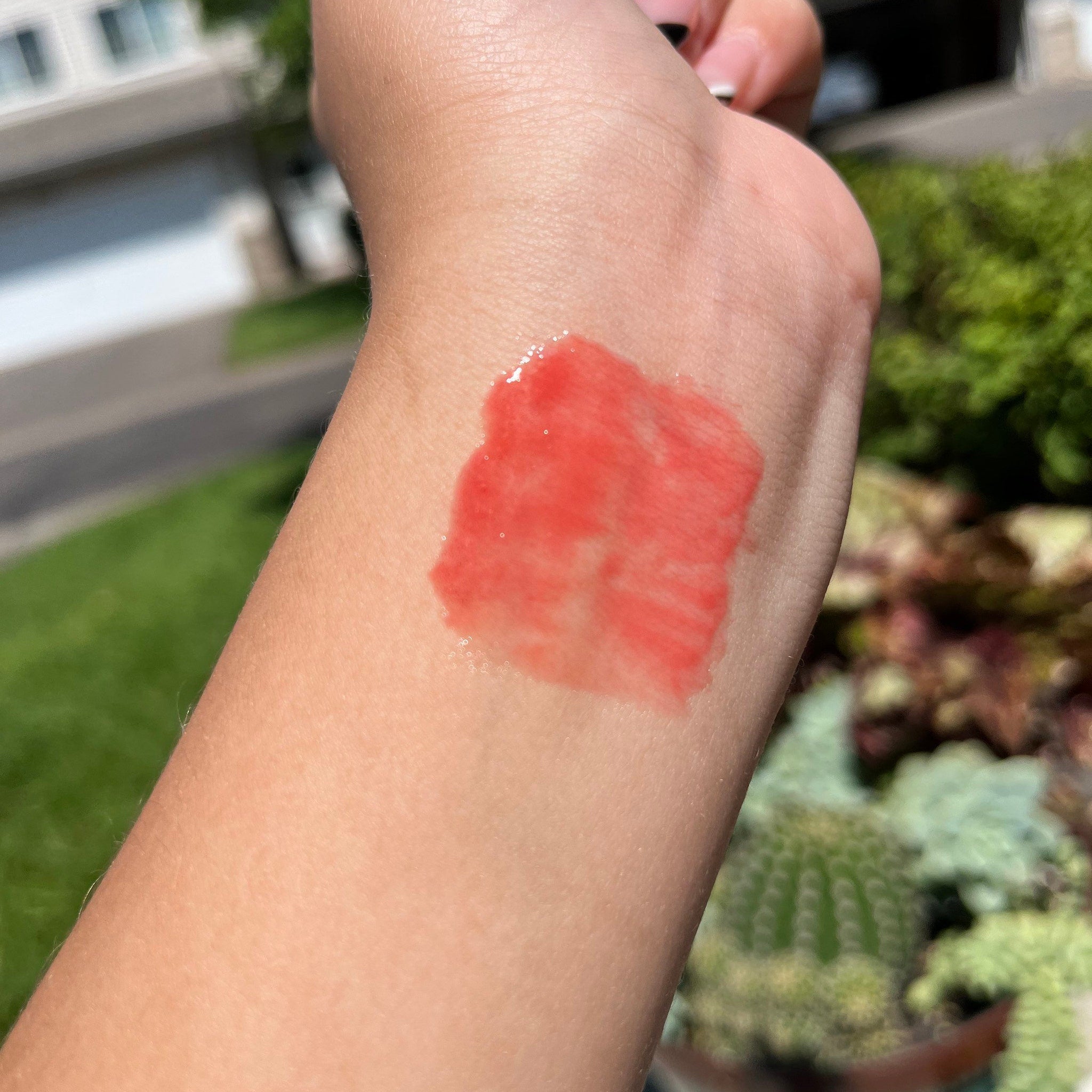 Lip gloss swatch, red-orange color, glossy finish, applied on skin