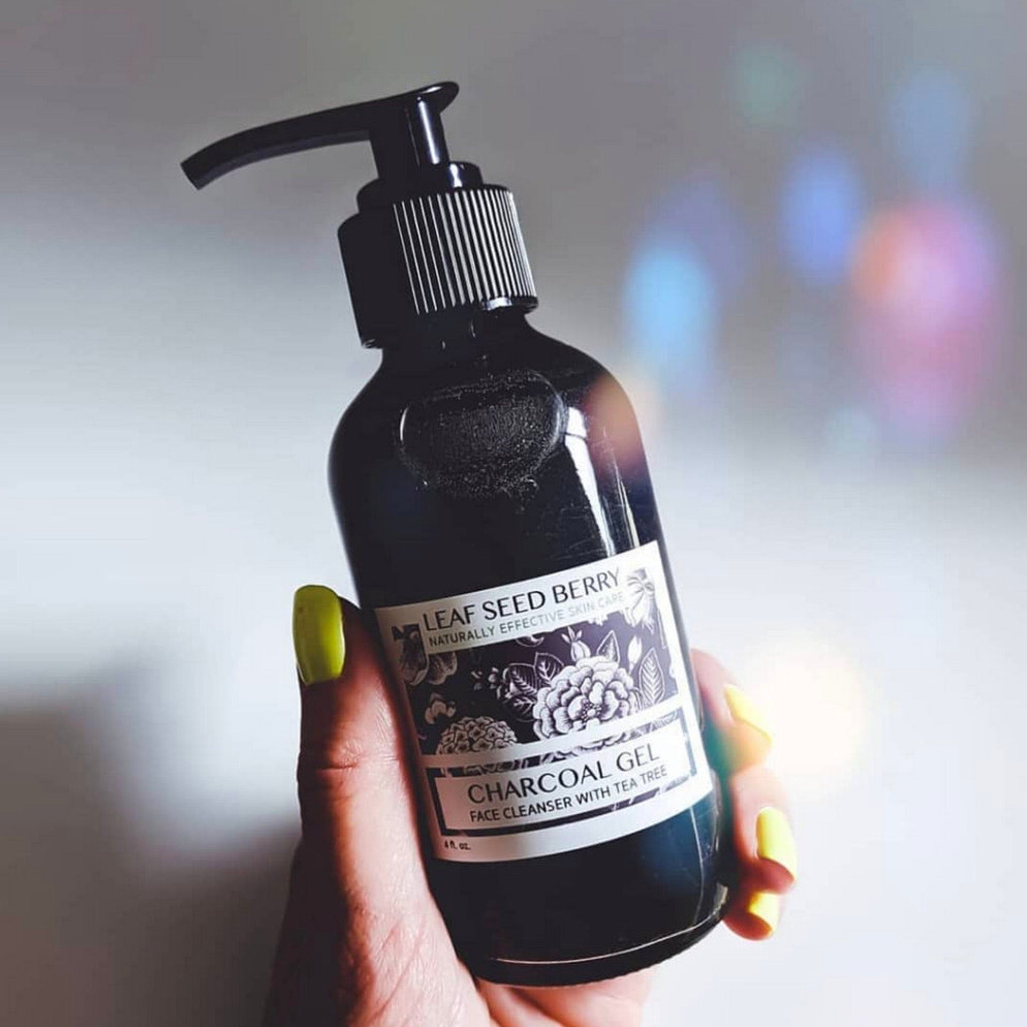 Charcoal gel bottle, black glass, white label, held in hand with yellow nails