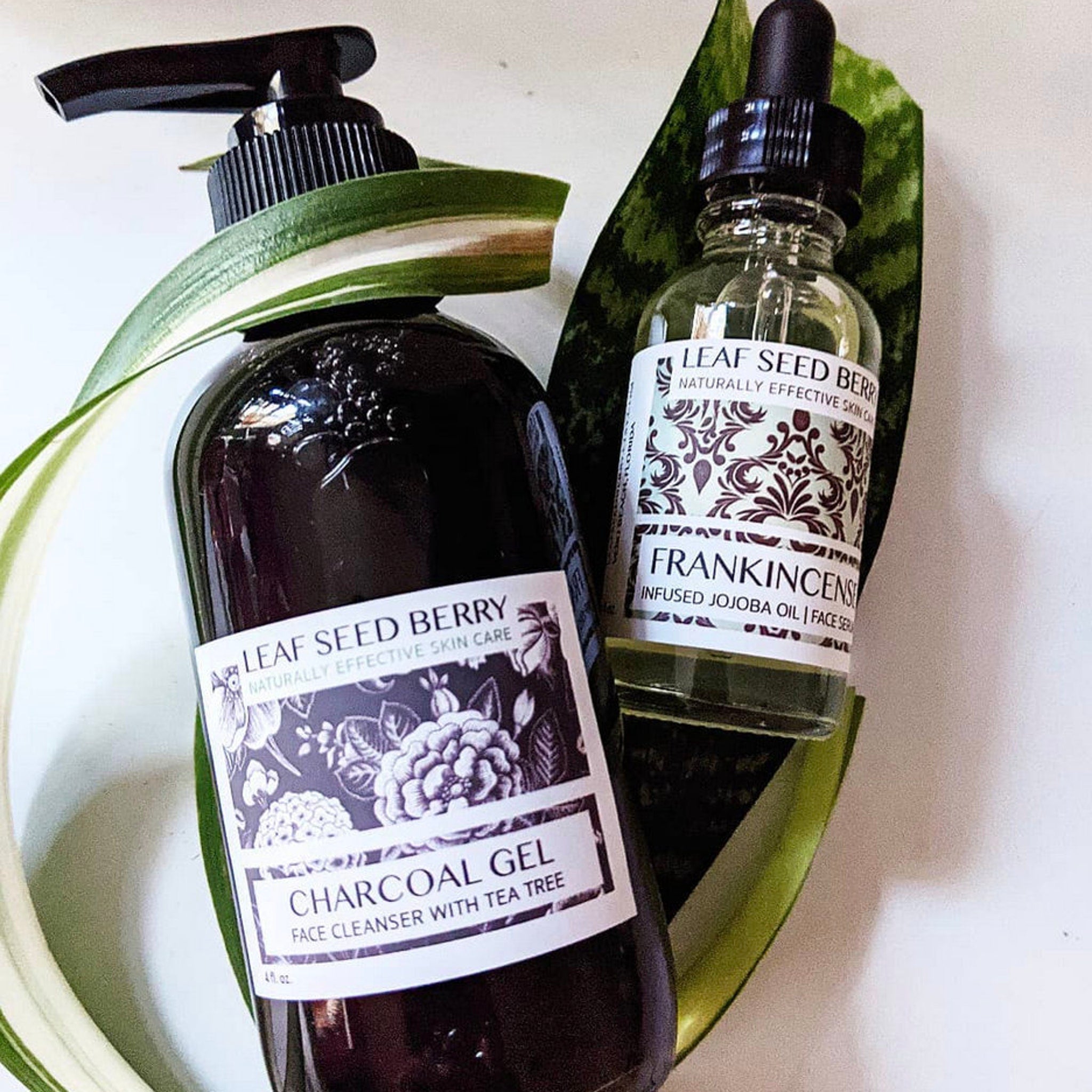 Face cleanser bottle with black pump and Leaf Seed Berry label, clear oil bottle with dropper, green leaves
