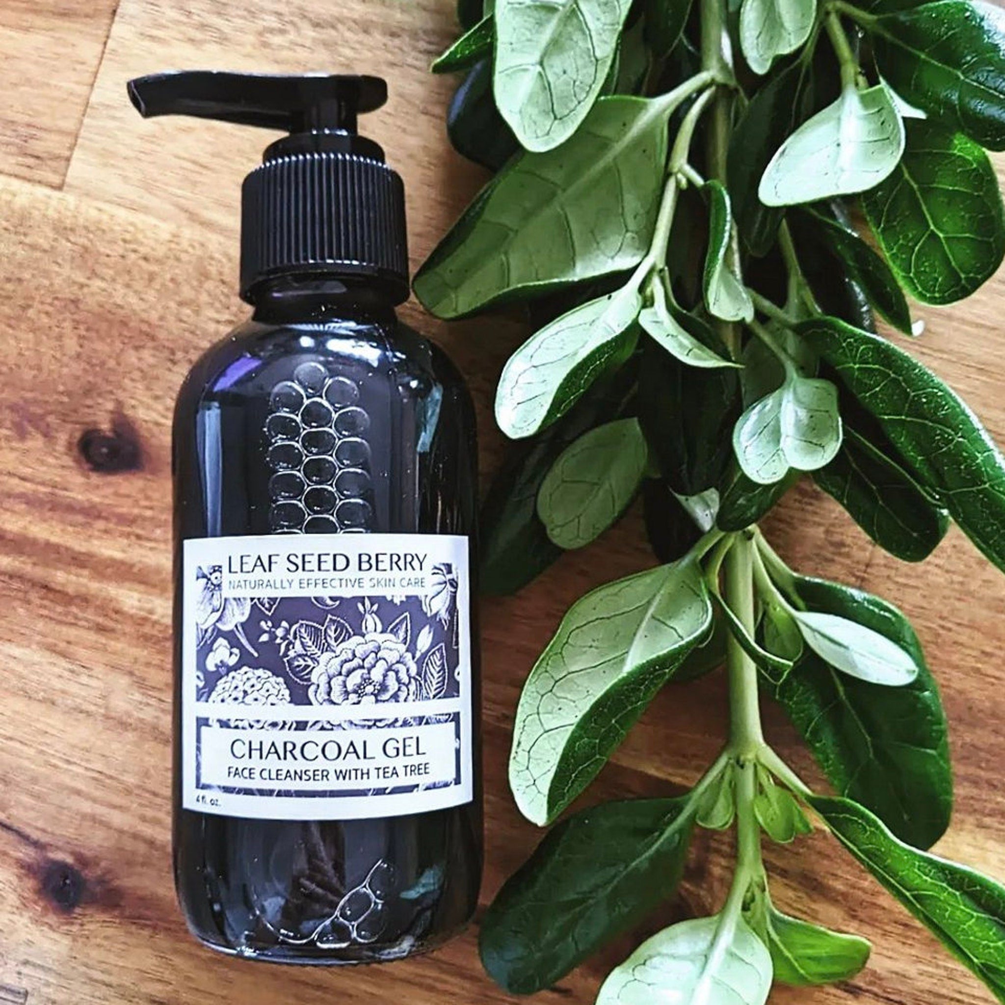 Charcoal gel face cleanser in black glass bottle with black pump and green leaves on wood surface