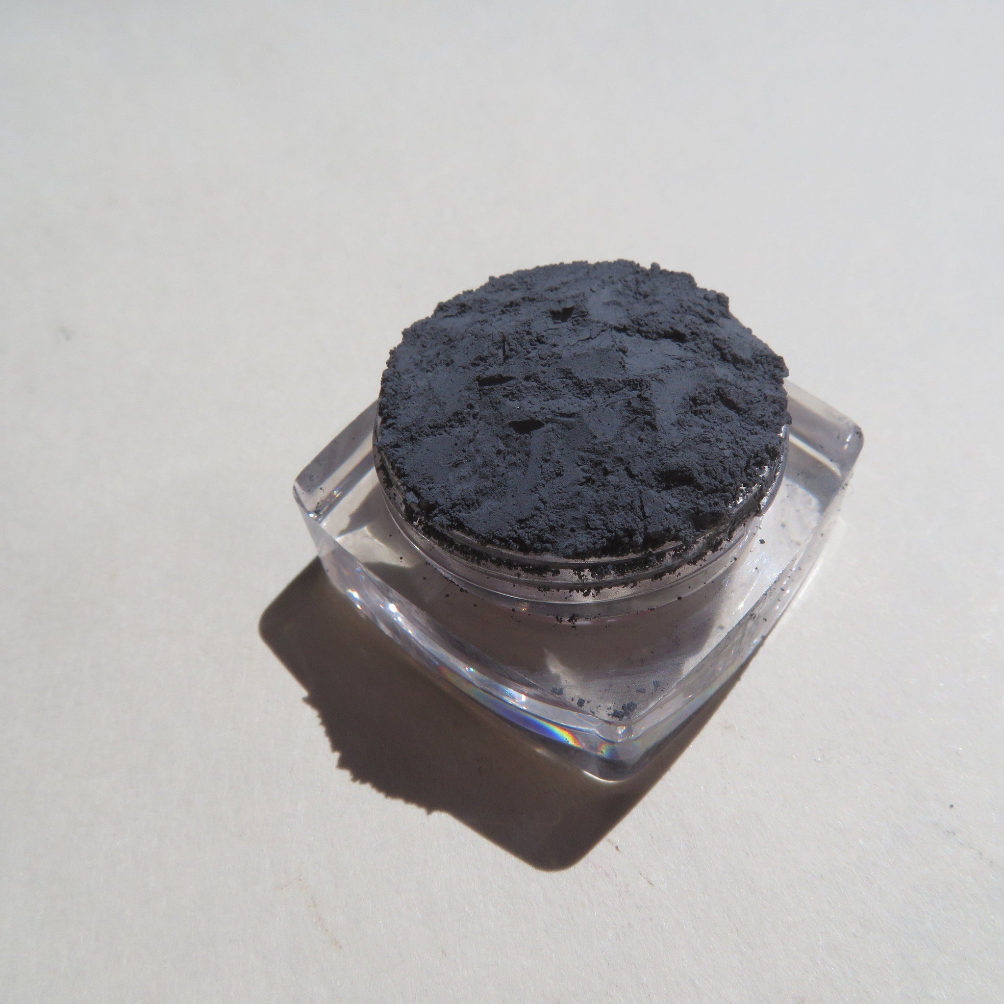 Powdered charcoal in clear plastic jar with dark gray powder and clear container