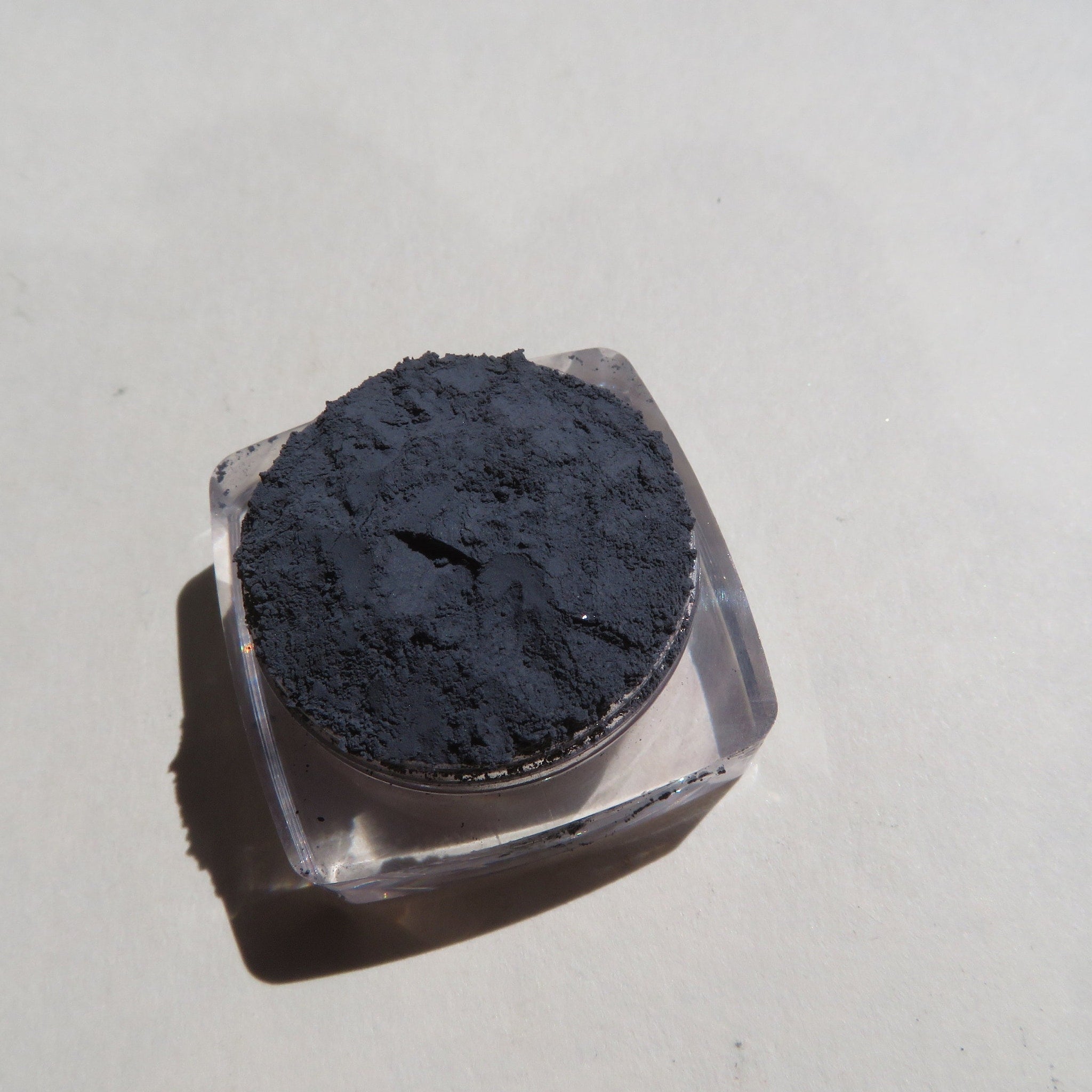 Black powder in clear plastic container, on light background, shadow visible