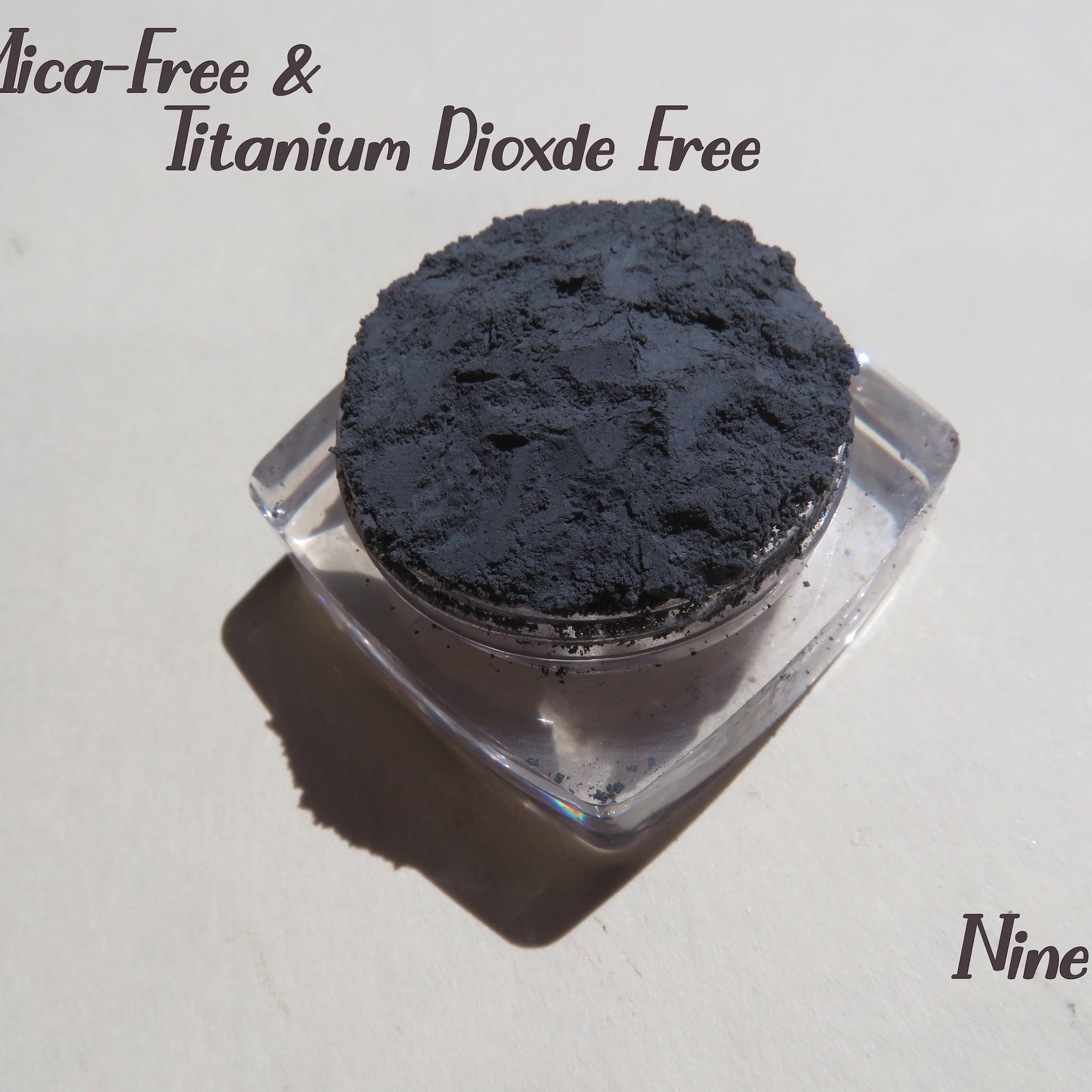 Dark gray powder in a clear plastic container, Nine brand name visible, Mica-Free & Titanium Dioxide Free text