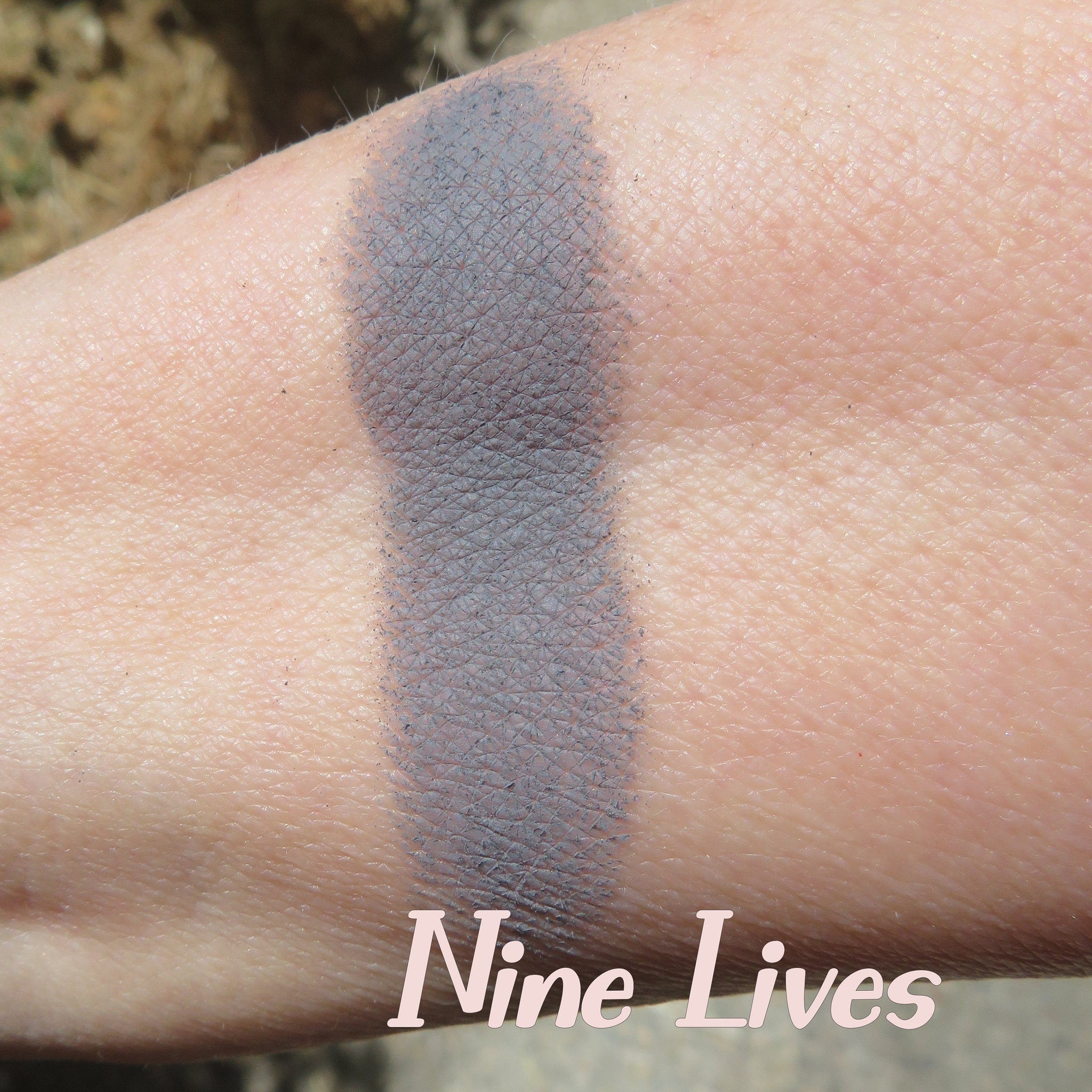 Side view of dark gray mica mineral eyeshadow powder spilling from jar onto brushed metal surface