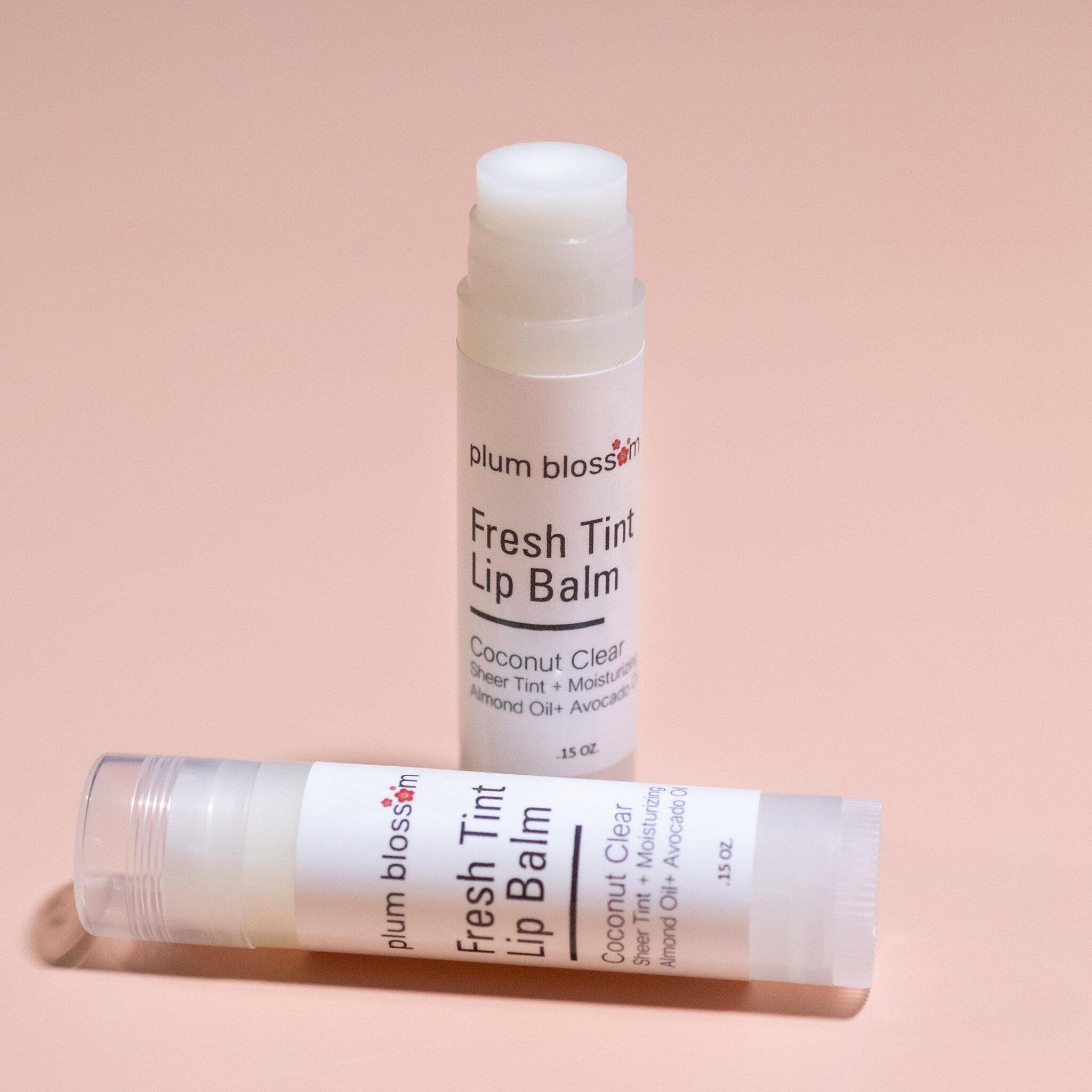 Lip balm tubes, white plastic with Plum Blossom Apothecary text, on pink background