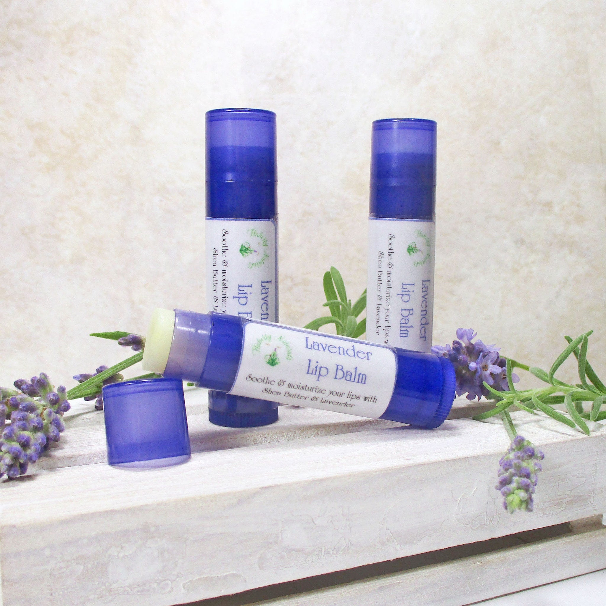Lavender lip balm tubes, blue and white label, with lavender sprigs on a white wooden surface