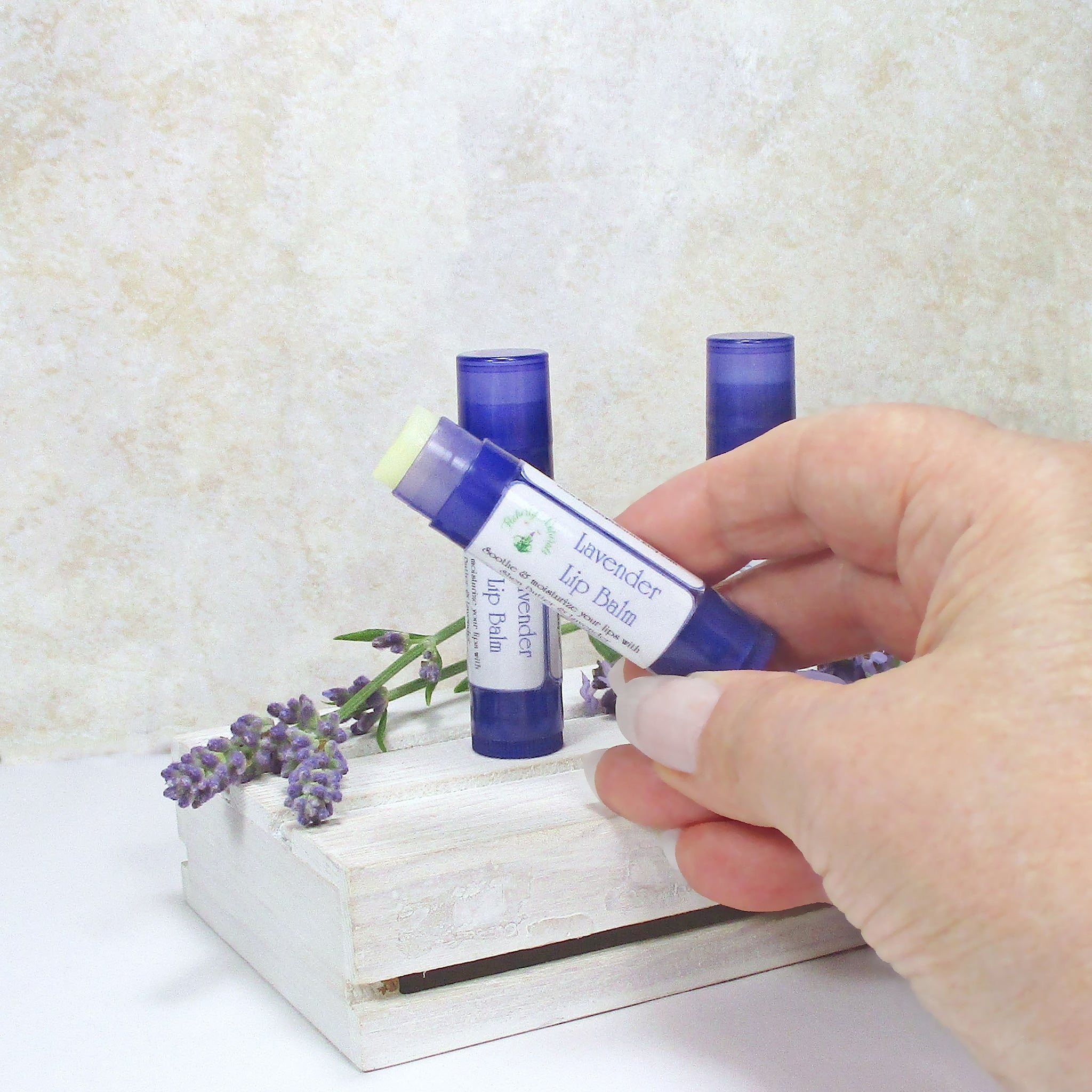 Lavender lip balm in blue tube with white label, held by hand with lavender sprig in background