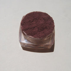 Close-up of matte dark brown purple mineral eyeshadow with loose pigment texture in a small jar