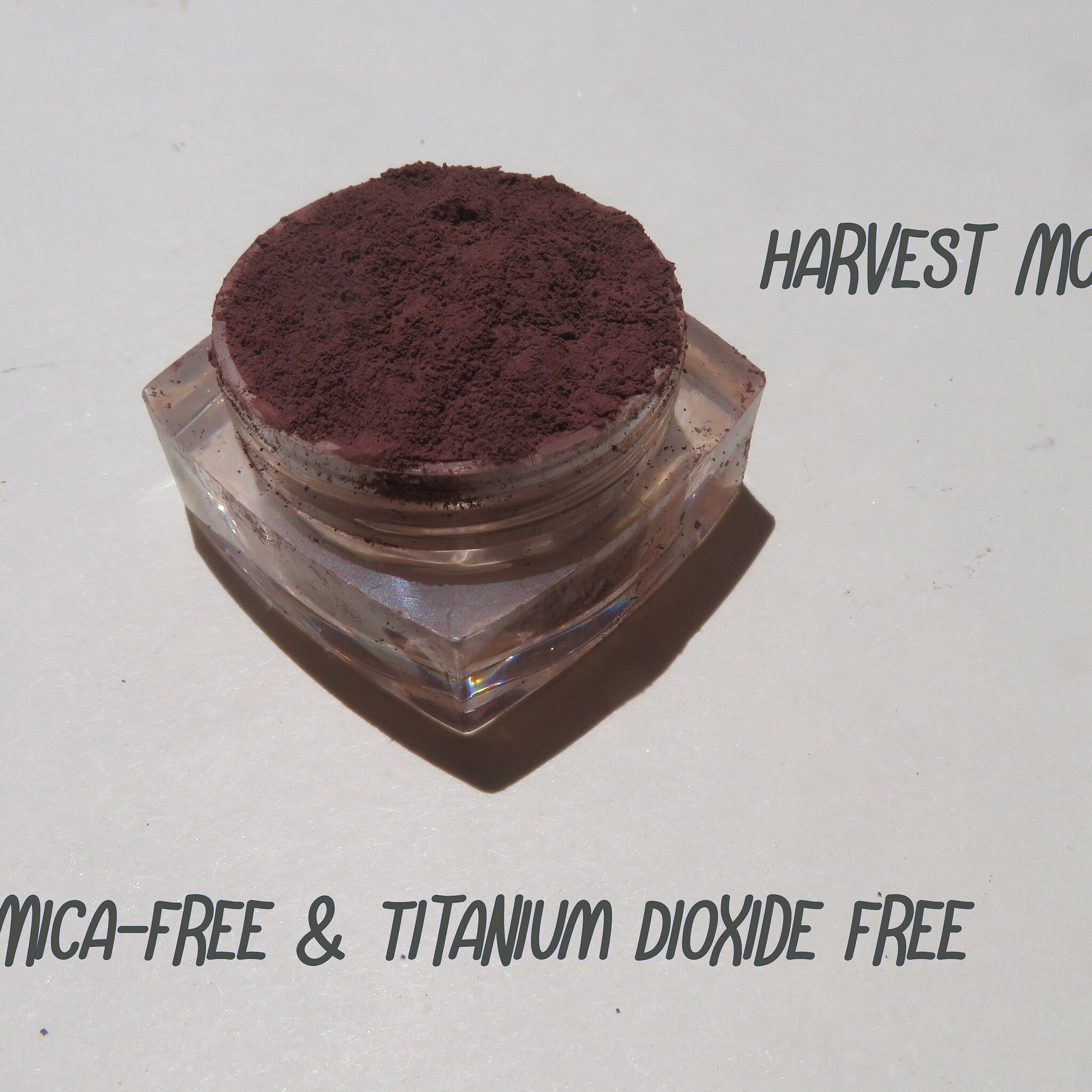 Close-up of matte dark brown purple mineral eyeshadow with loose pigment texture in a small jar