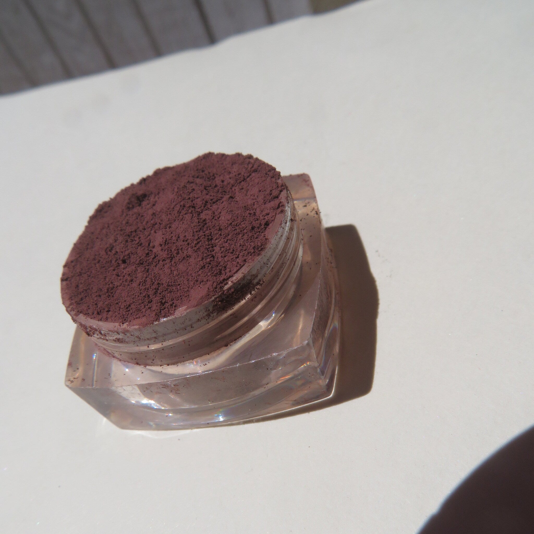Side view of matte dark brown purple mineral eyeshadow in loose powder form with vegan cruelty-free label visible