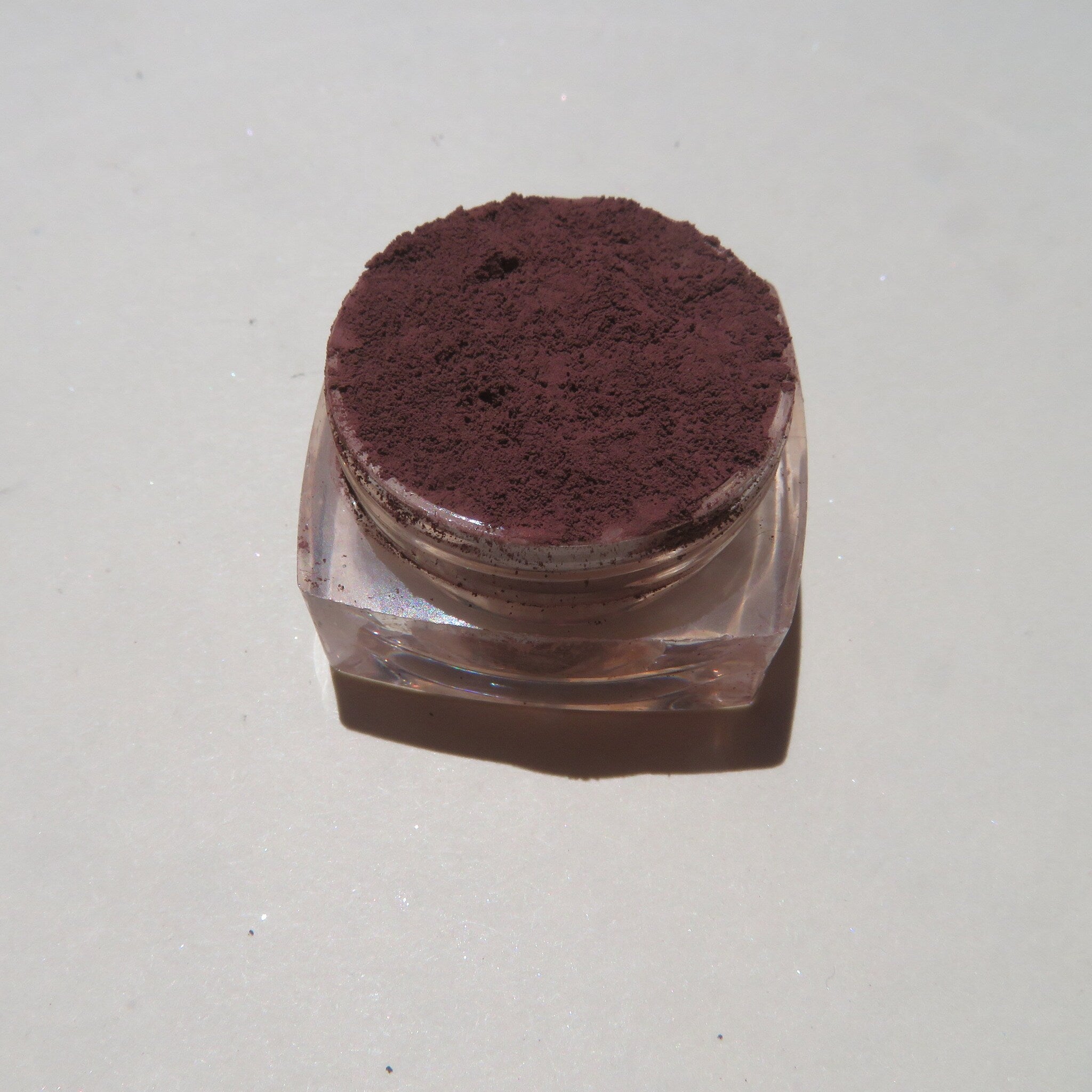 Side view of matte dark brown purple mineral eyeshadow in loose powder form with vegan cruelty-free label