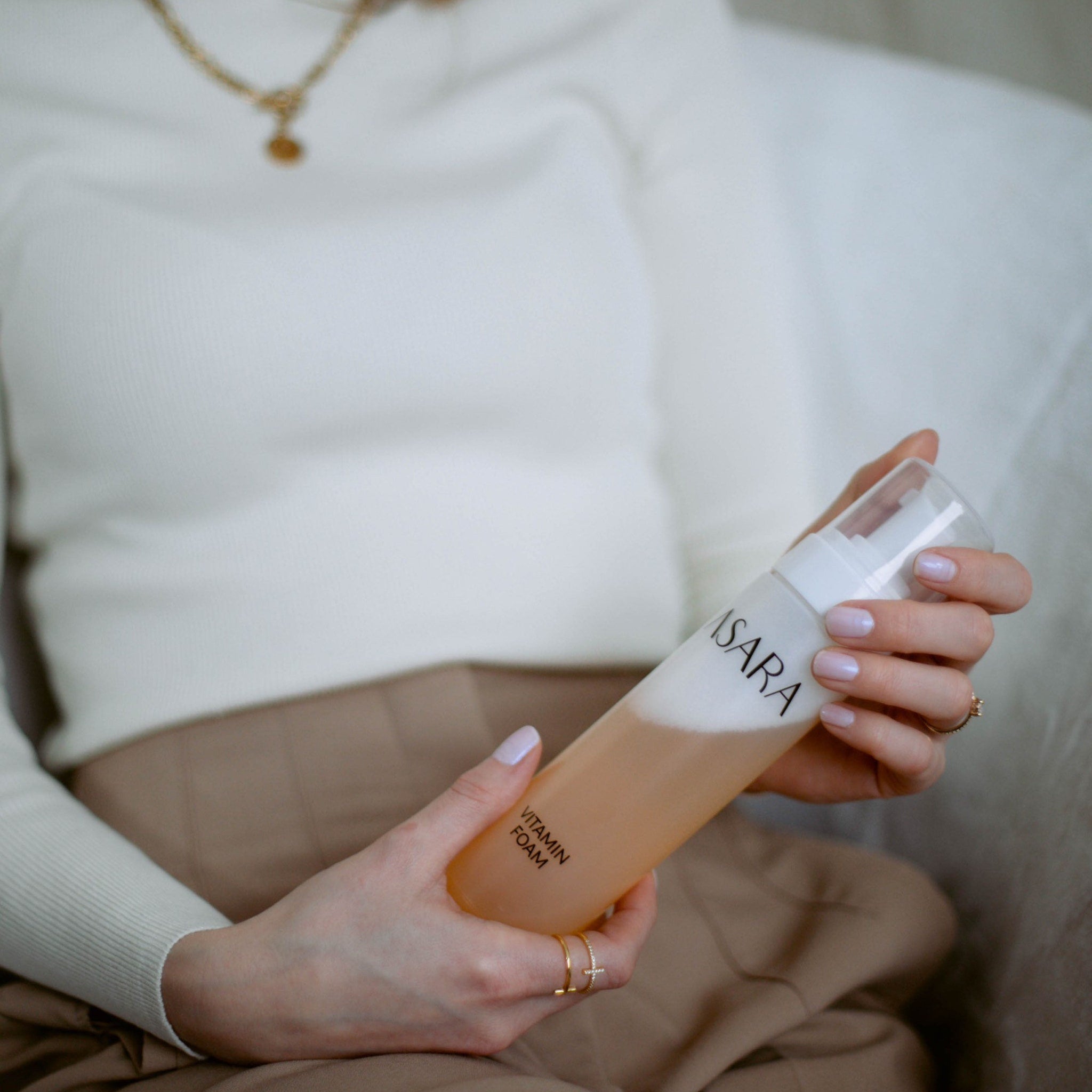 Vitamin foam bottle held in hands, clear plastic, orange liquid, white foam, "ASARA" brand text