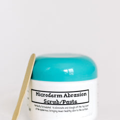 Microderm Abrasion Scrub/Paste in white jar with teal lid and wooden applicator next to it