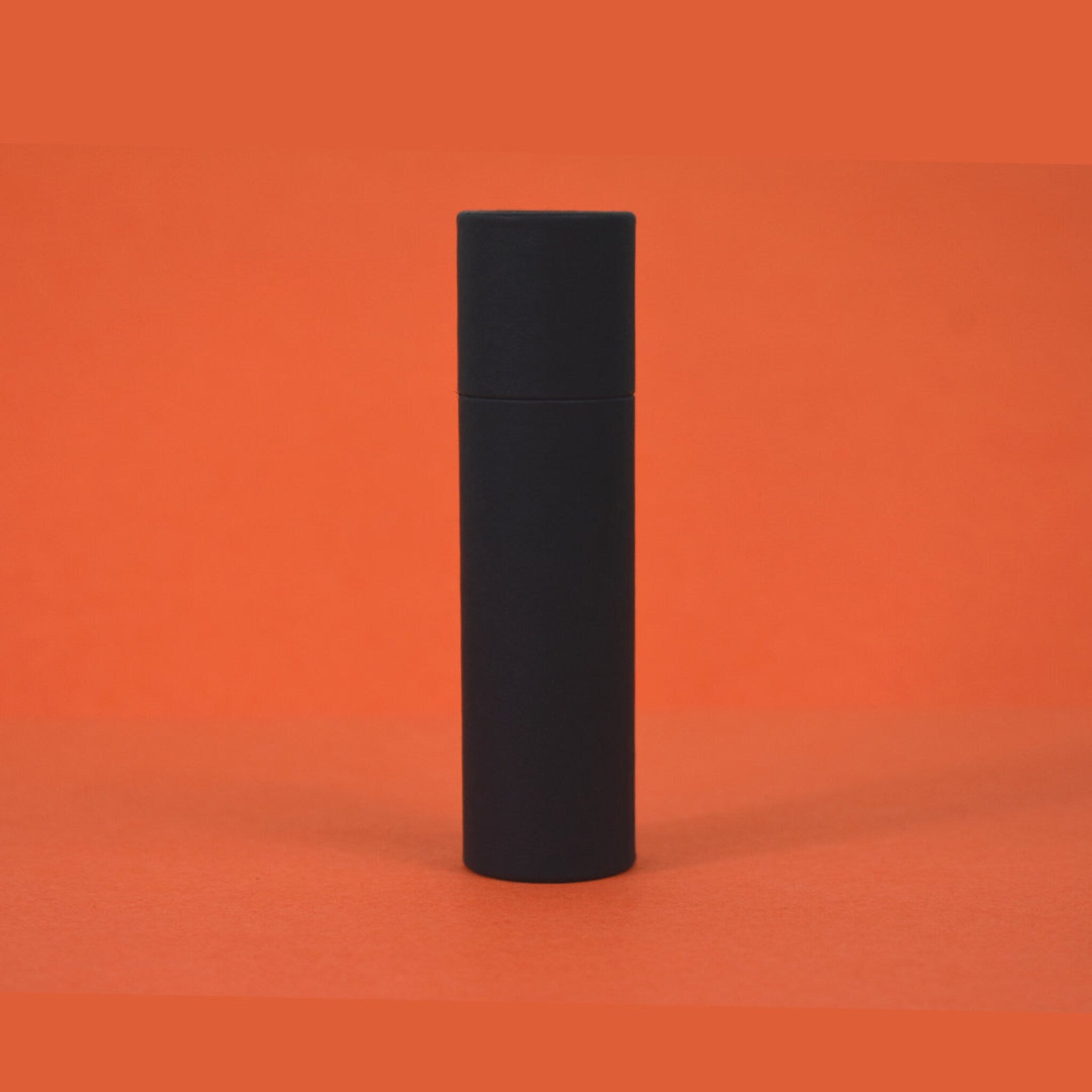 Black cylindrical container on orange background, matte finish, minimalist design
