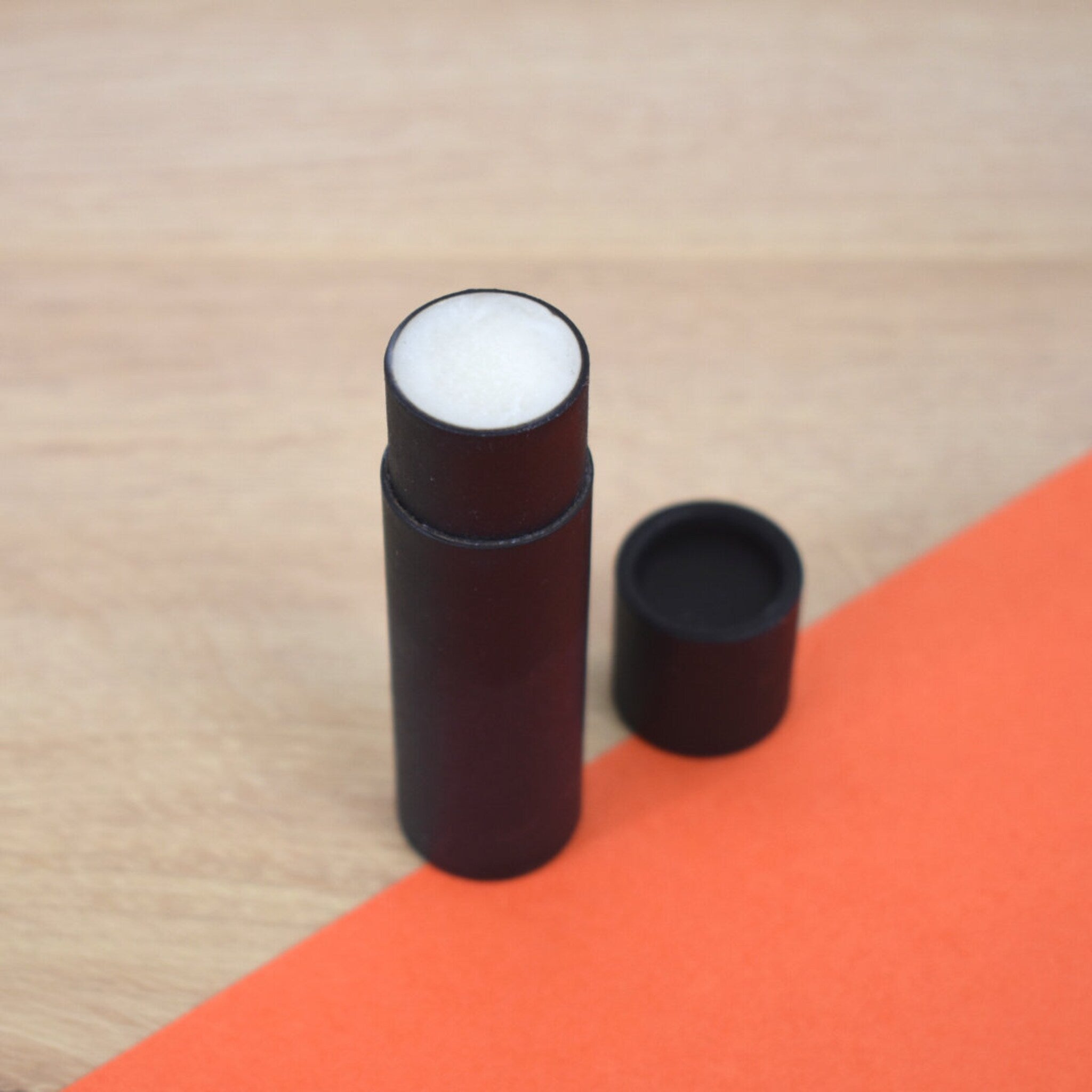 Lip balm tube with black paper tube, white balm, and black cap on orange background