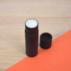 Lip balm tube with black paper tube, white balm, and black cap on orange background