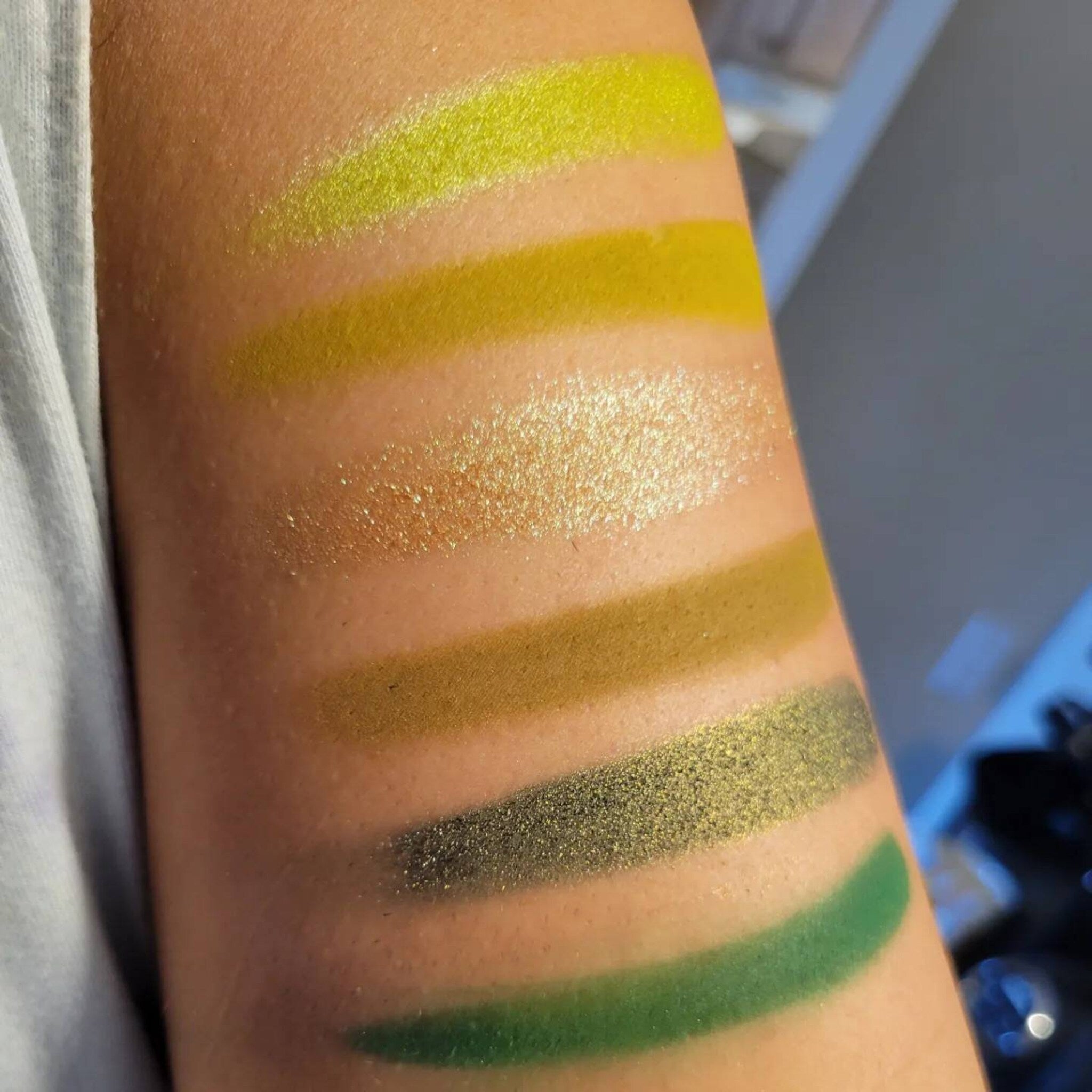 Close-up of six matte green eyeshadow pans in earthy herb shades with smooth powder texture