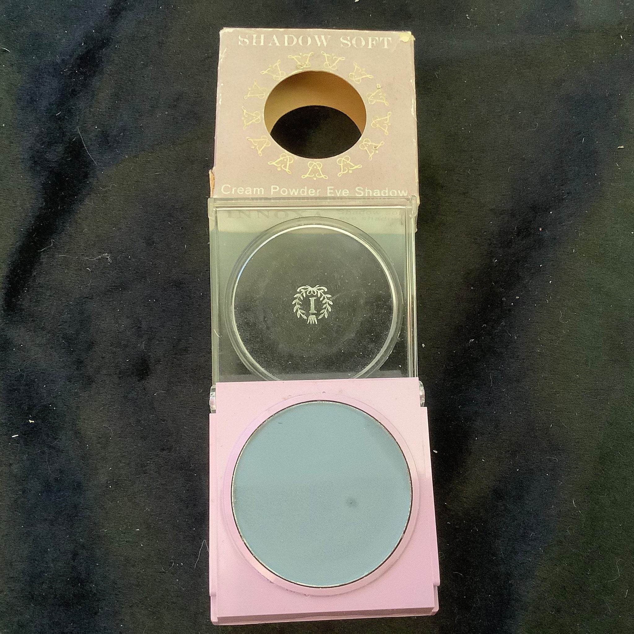 Eye shadow compact with blue powder, pink case, and clear lid with brand name visible