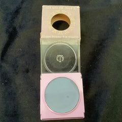 Eye shadow compact with blue powder, pink case, and clear lid with brand name visible