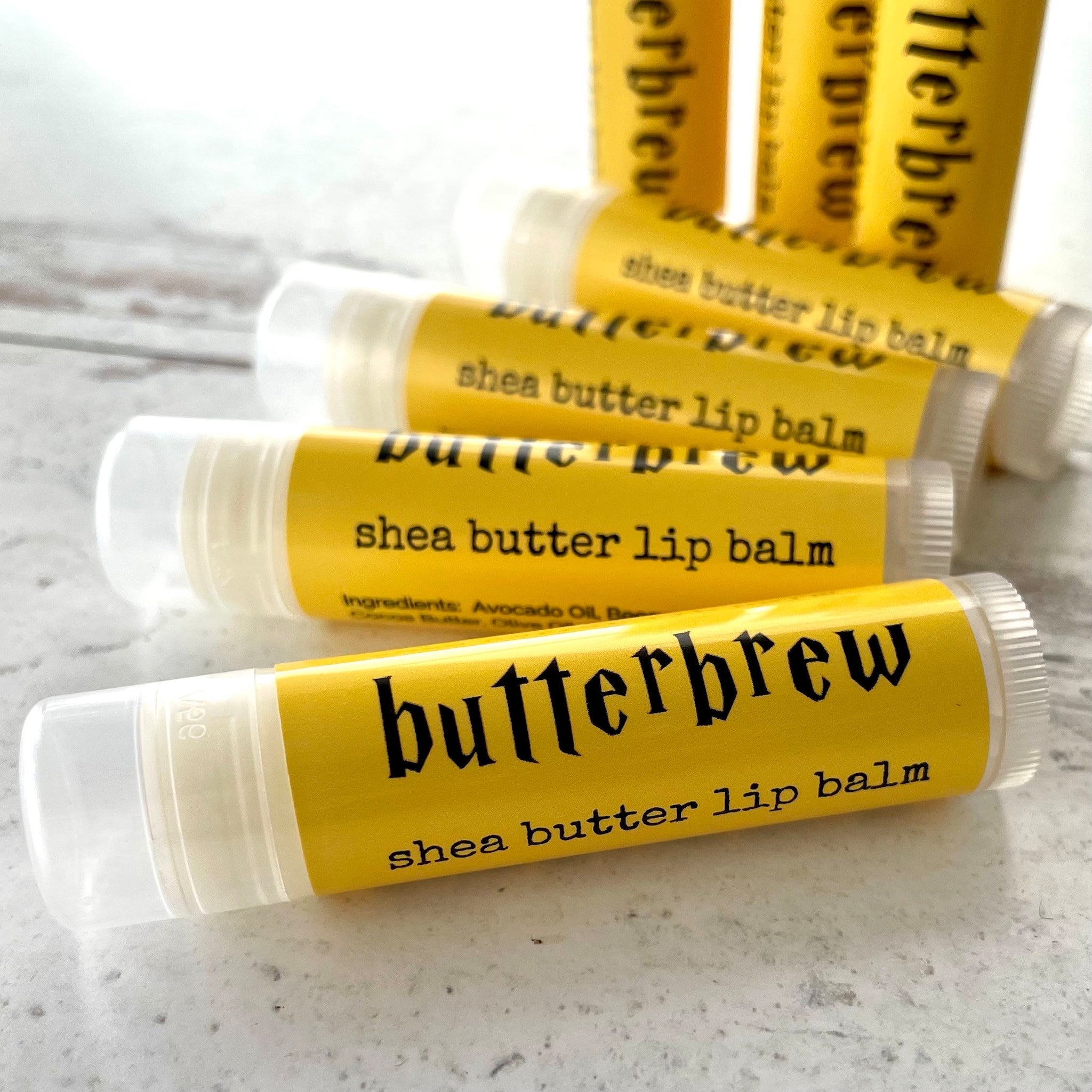 Shea butter lip balm in yellow and white tubes with black text, Butterbrew brand visible
