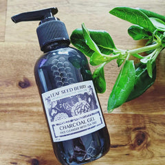 Charcoal gel face cleanser bottle, black glass, Leaf Seed Berry label, with green leaves on wood surface