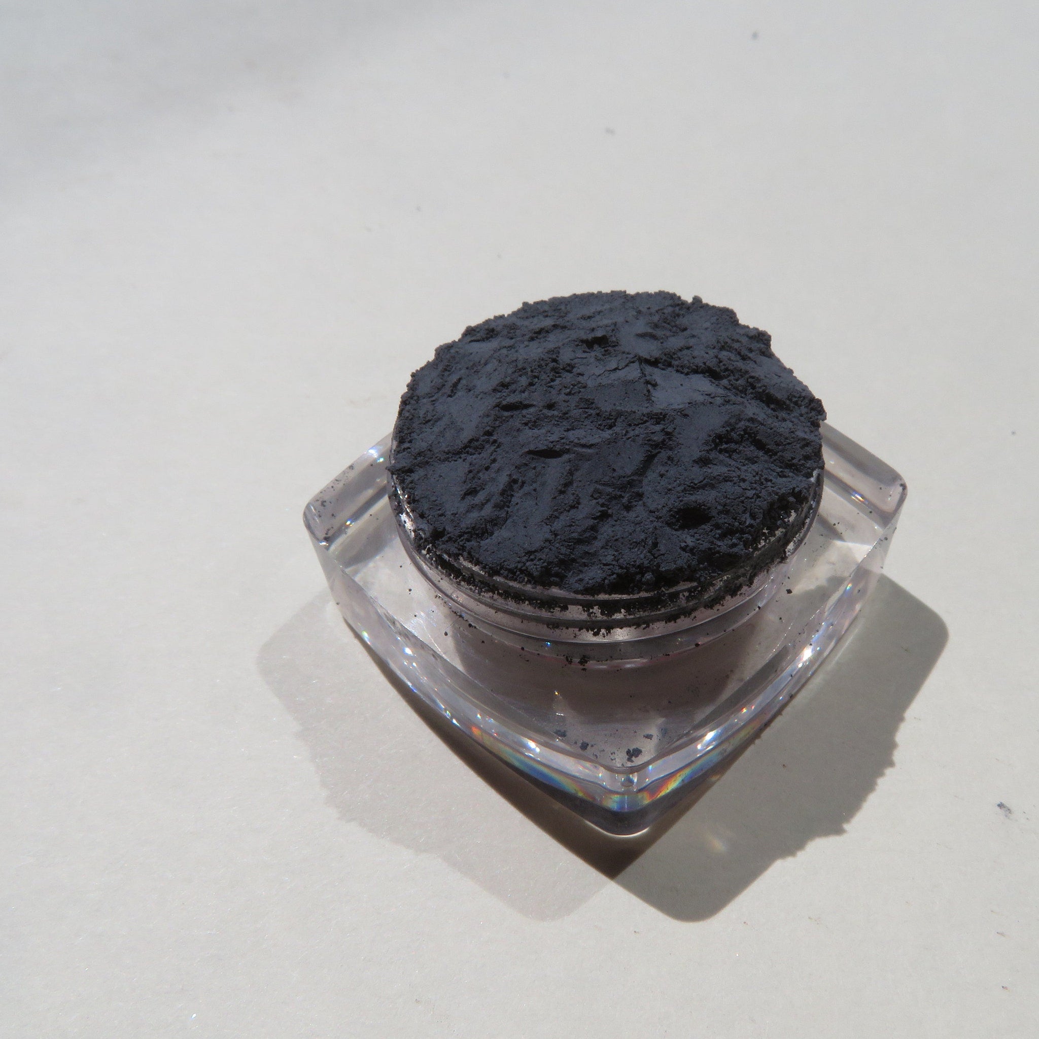 Dark powder in clear plastic container, with black powder and translucent container, on a white surface