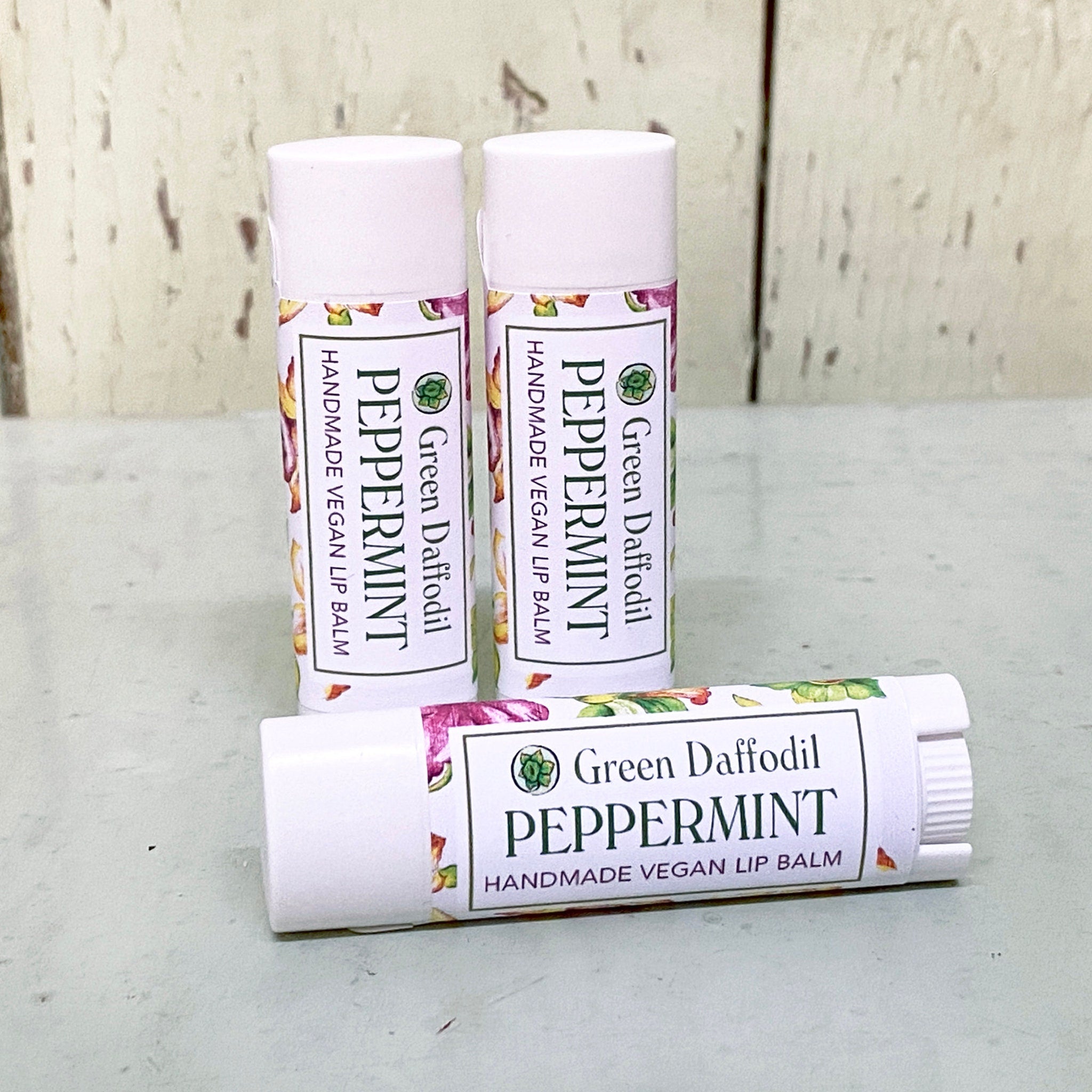 Lip balm tubes, white with floral labels, Green Daffodil peppermint, three tubes on surface