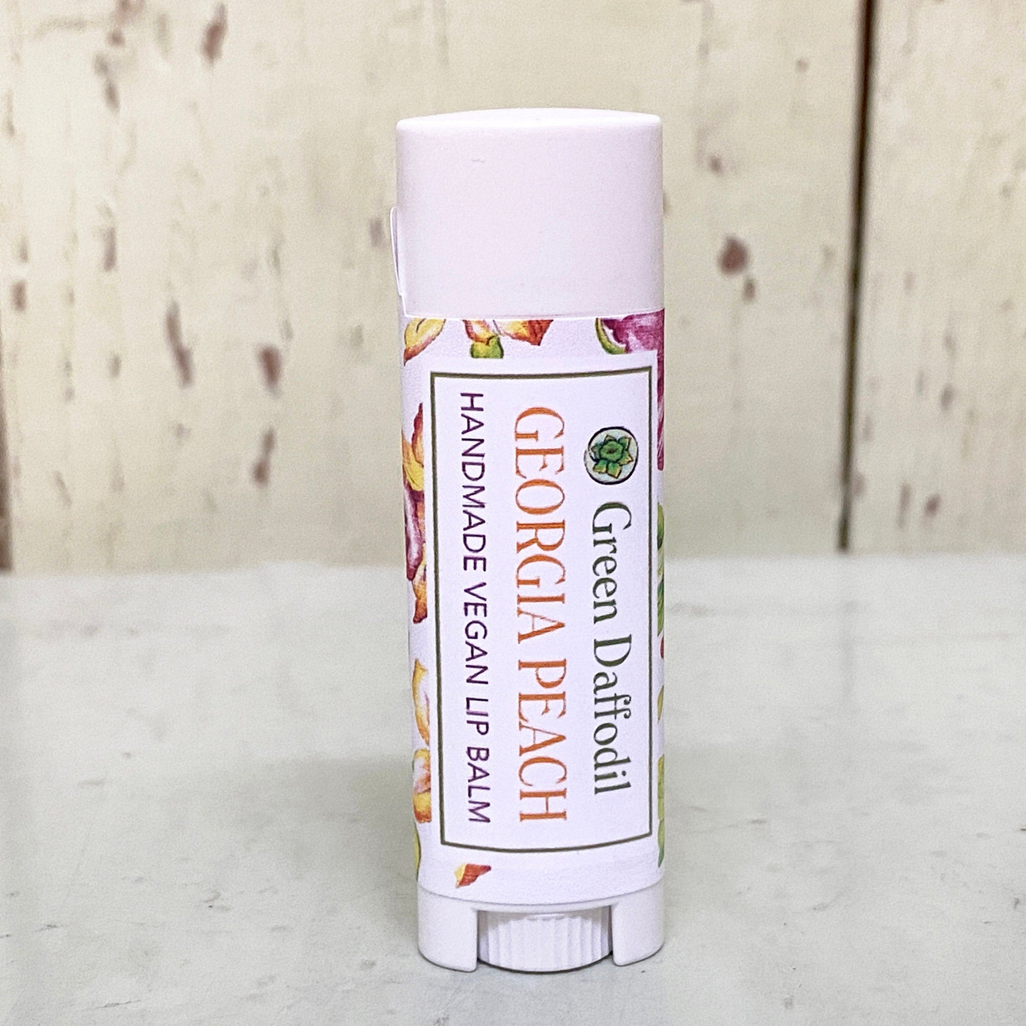 Lip balm tube with white cap, floral label, and "Georgia Peach" text visible
