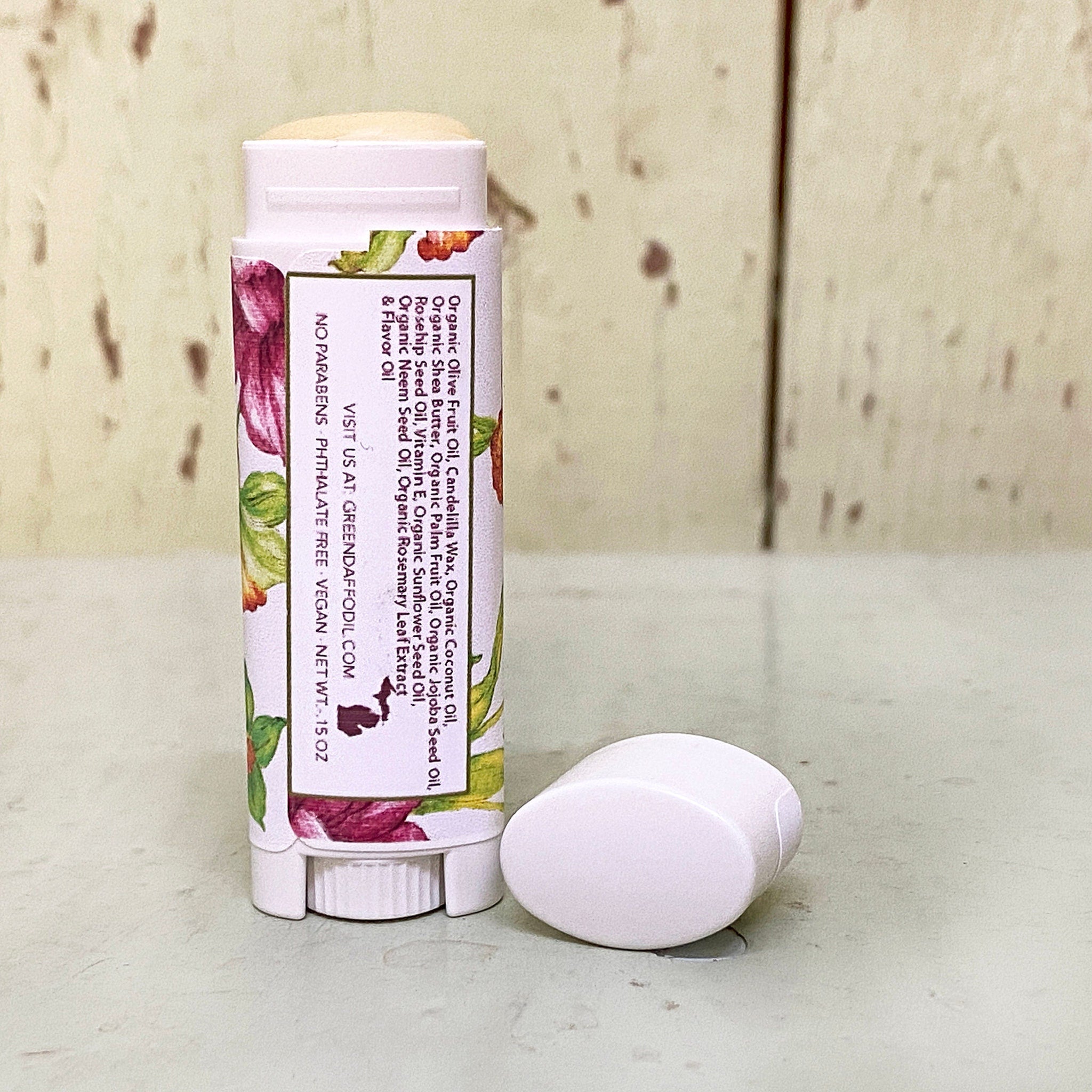 Lip balm stick with white tube, floral pattern, and white cap next to it