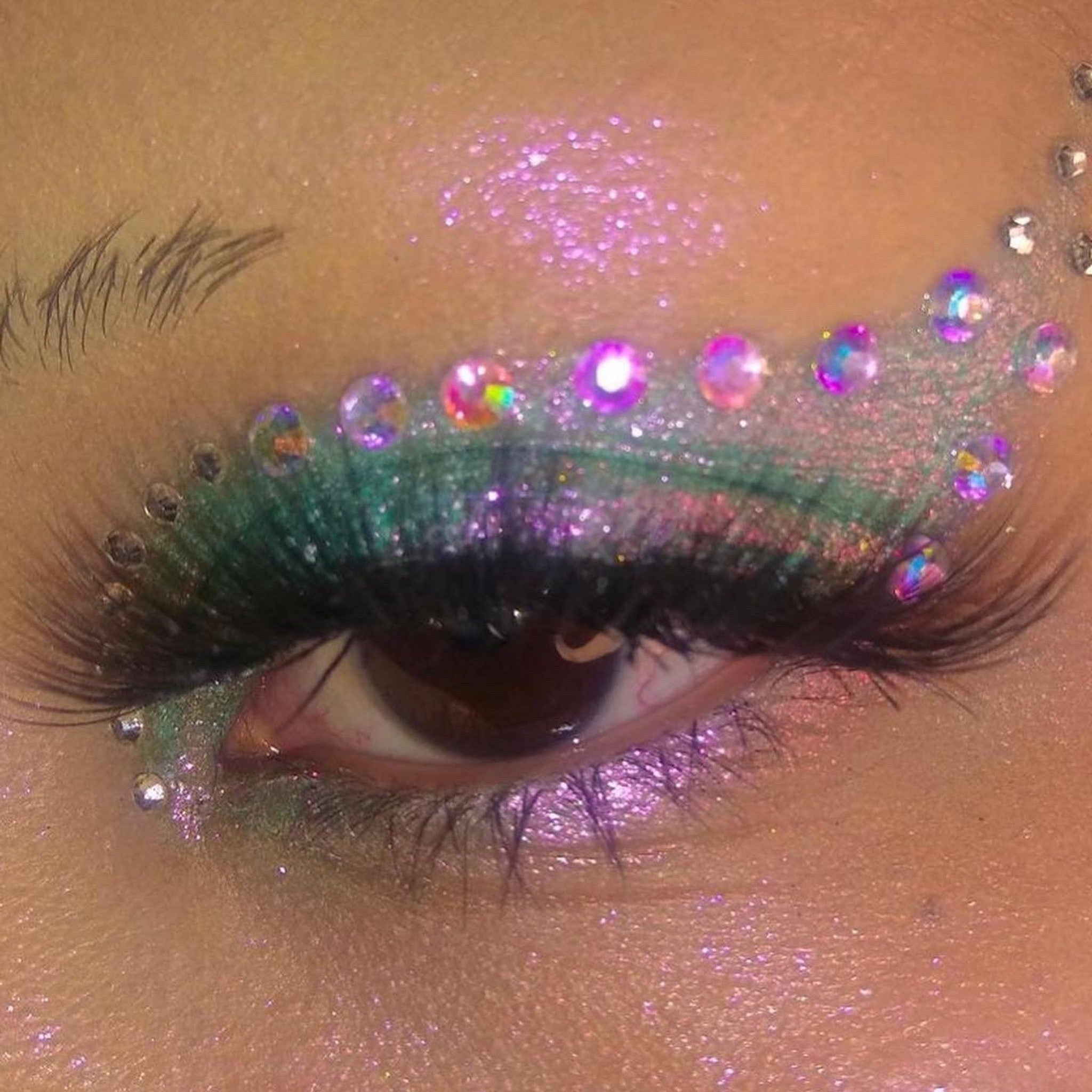 Eye makeup with green and purple glitter, and iridescent gems, close-up view of eye.