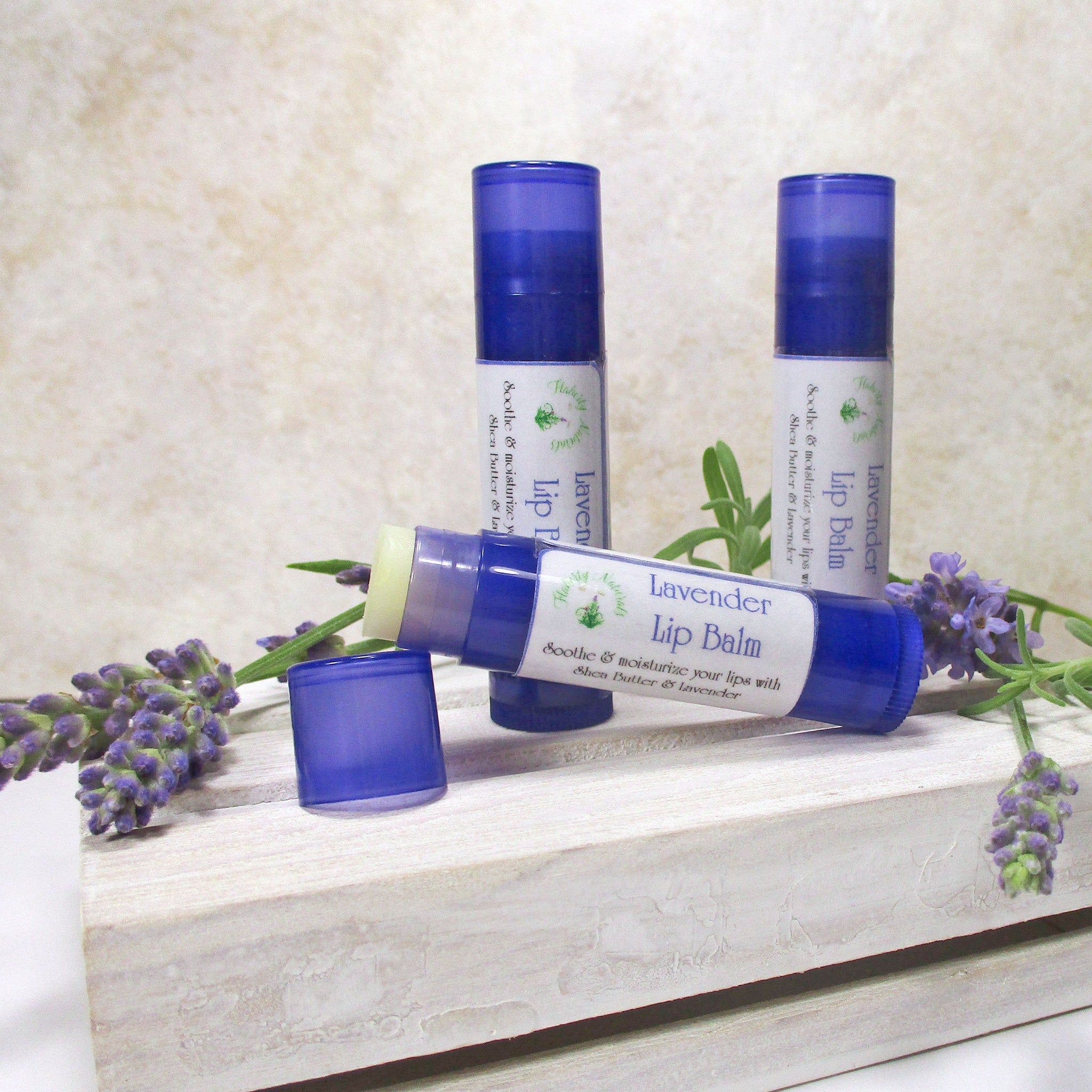 Lip balm tubes, blue and white with lavender, on a white wooden crate with lavender sprigs