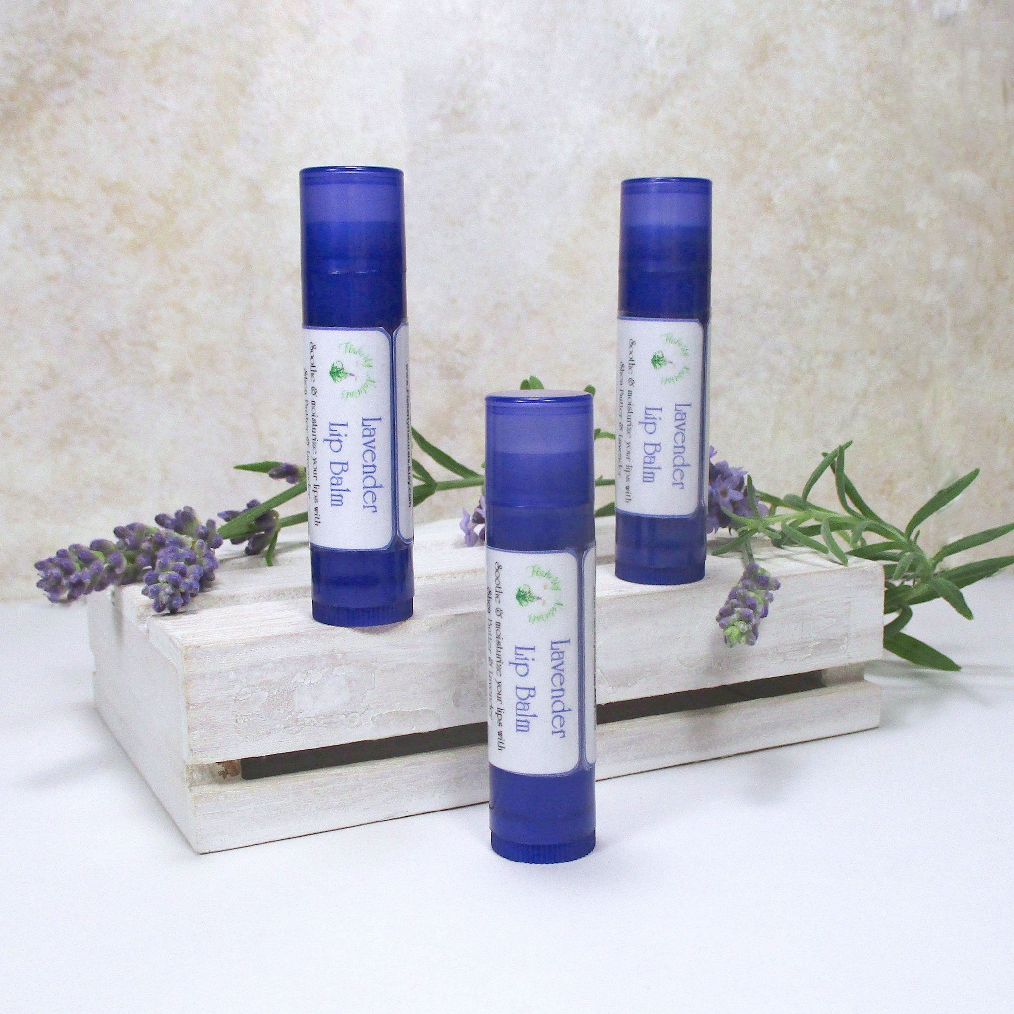 Lavender lip balm tubes, blue plastic, white label with text, displayed on white wood crate