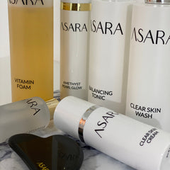 Skincare products in white bottles with black text, ASARA brand visible, and a black gua sha tool on a marble surface