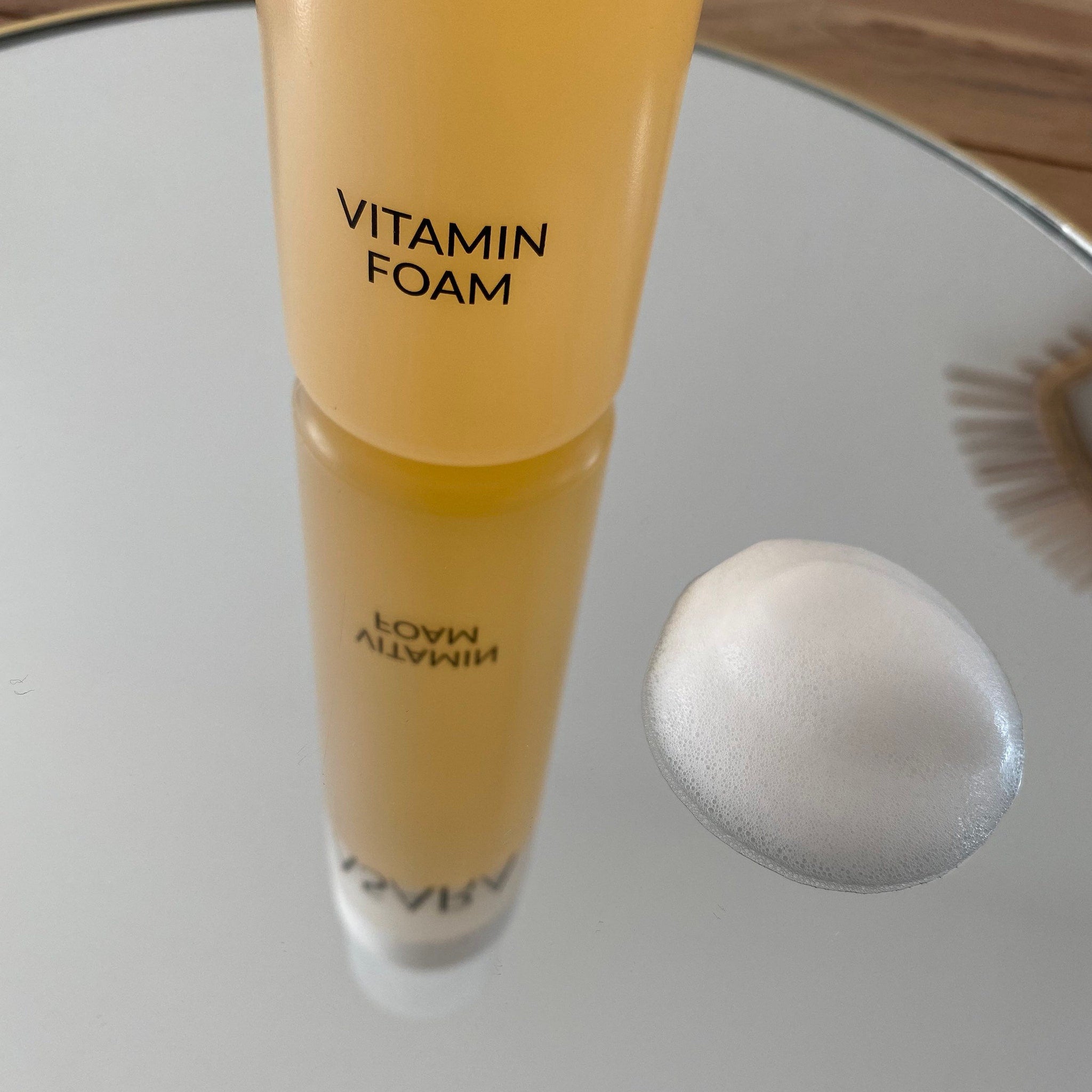 Vitamin foam, yellow bottle with black text, white foam on reflective surface