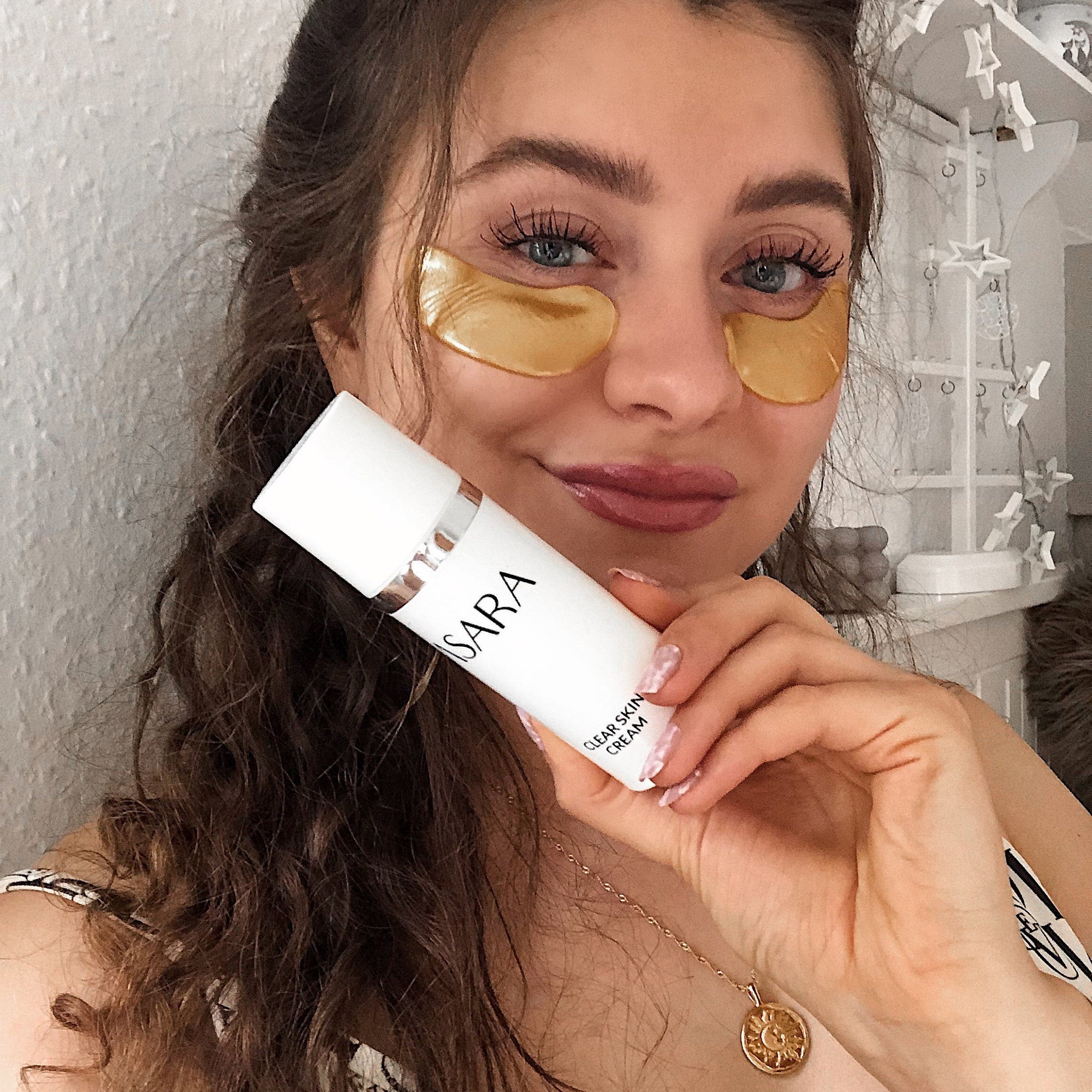 Skincare cream bottle held by woman, white container, "ISARA" brand, "Clear Skin Cream" text