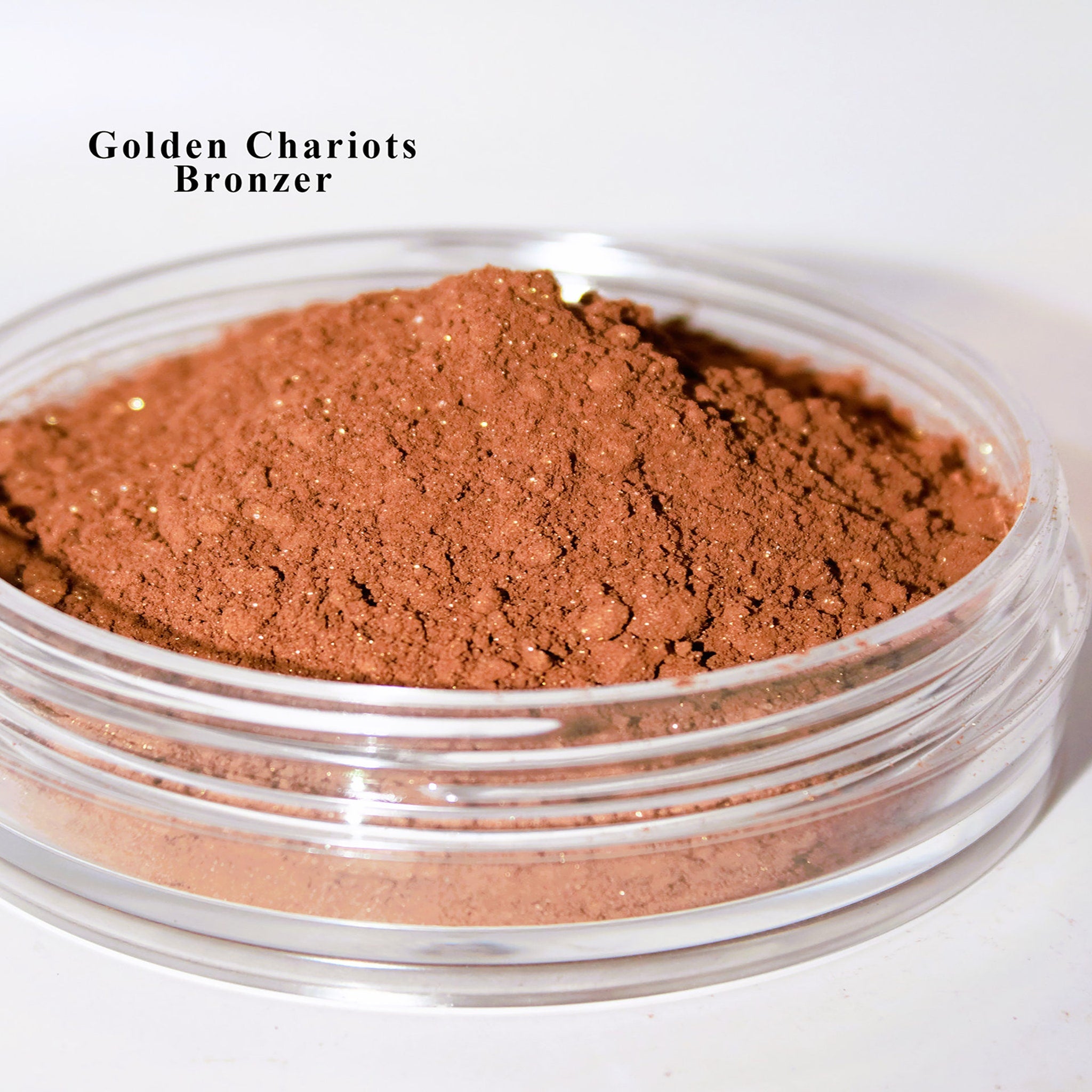 Bronzer powder, brown with gold flecks, in a clear plastic jar, Golden Chariots brand name visible