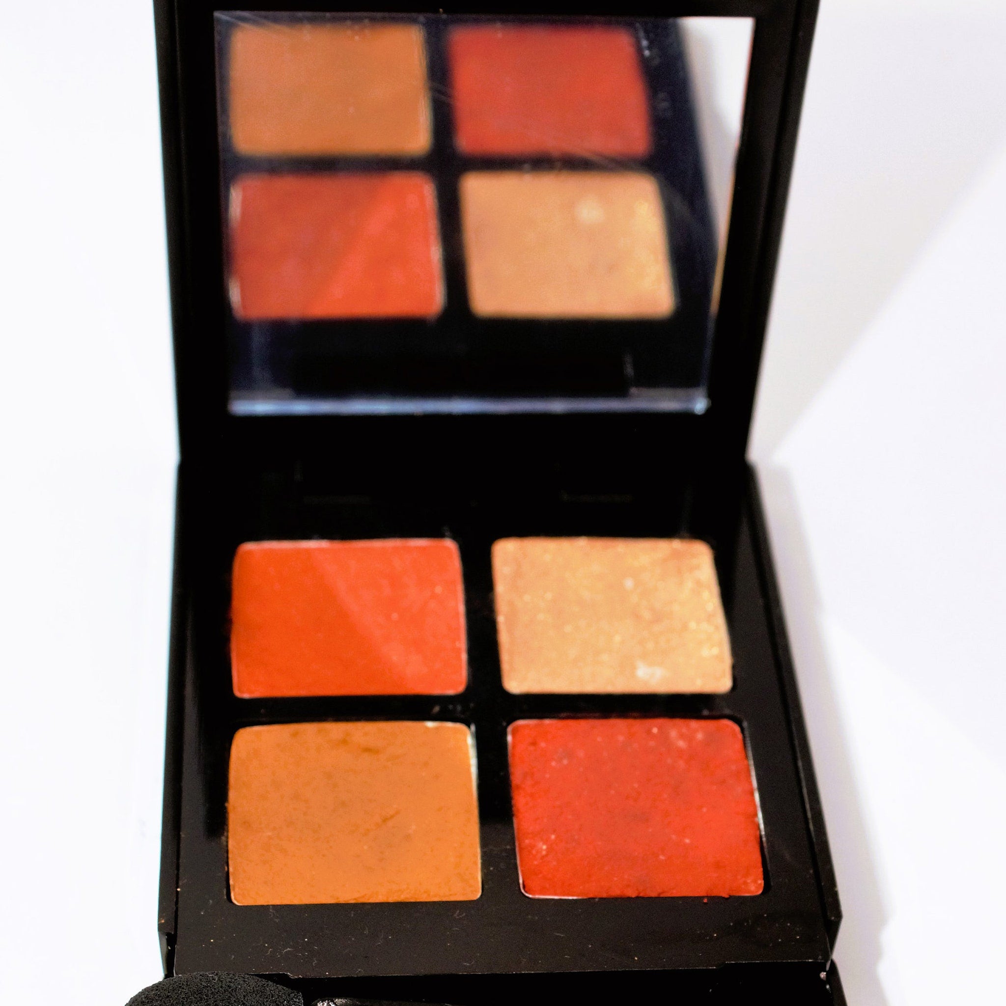 Eyeshadow palette with orange and peach shades in a black compact with mirror