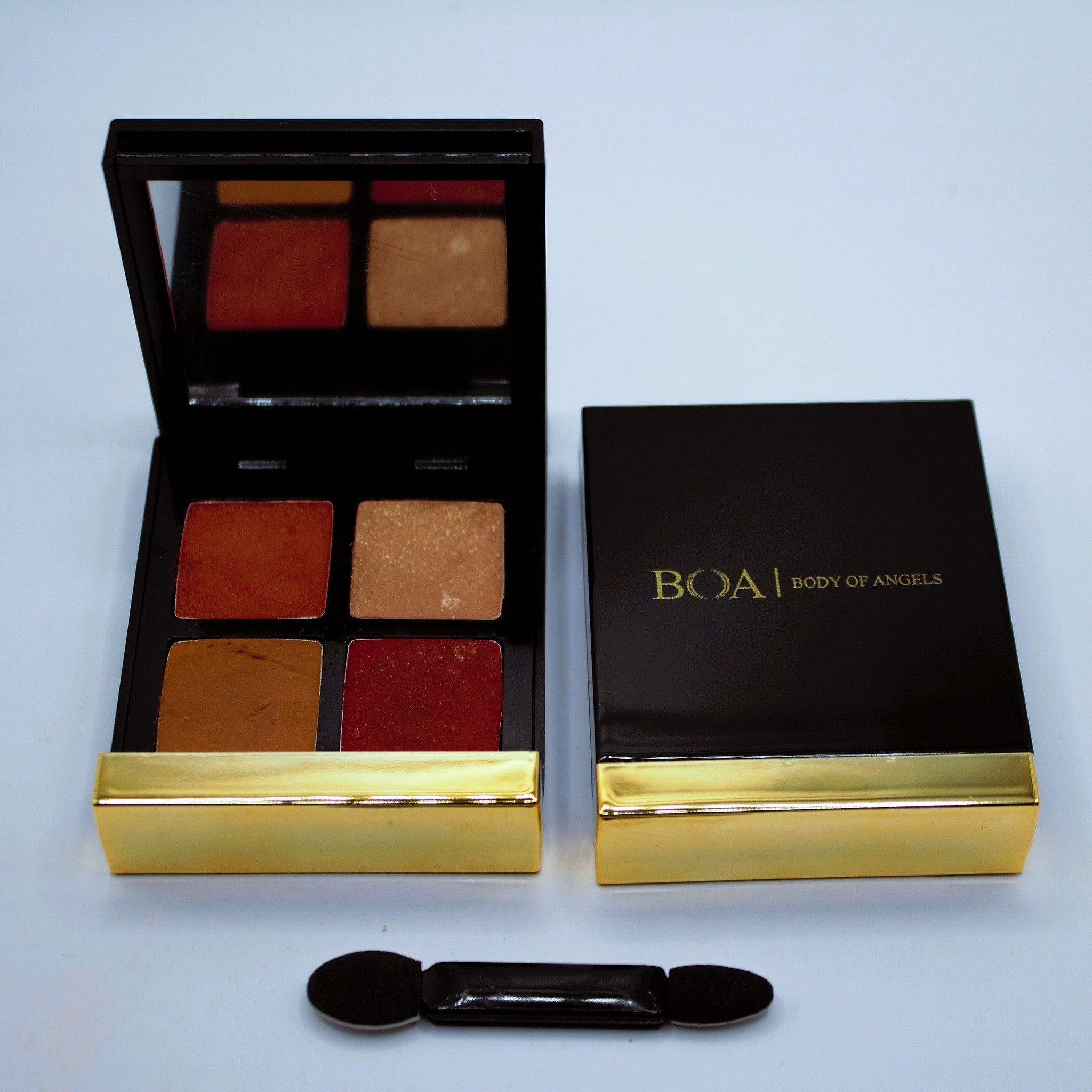 Eyeshadow palette with black and gold case, four shades of brown and red, and applicator