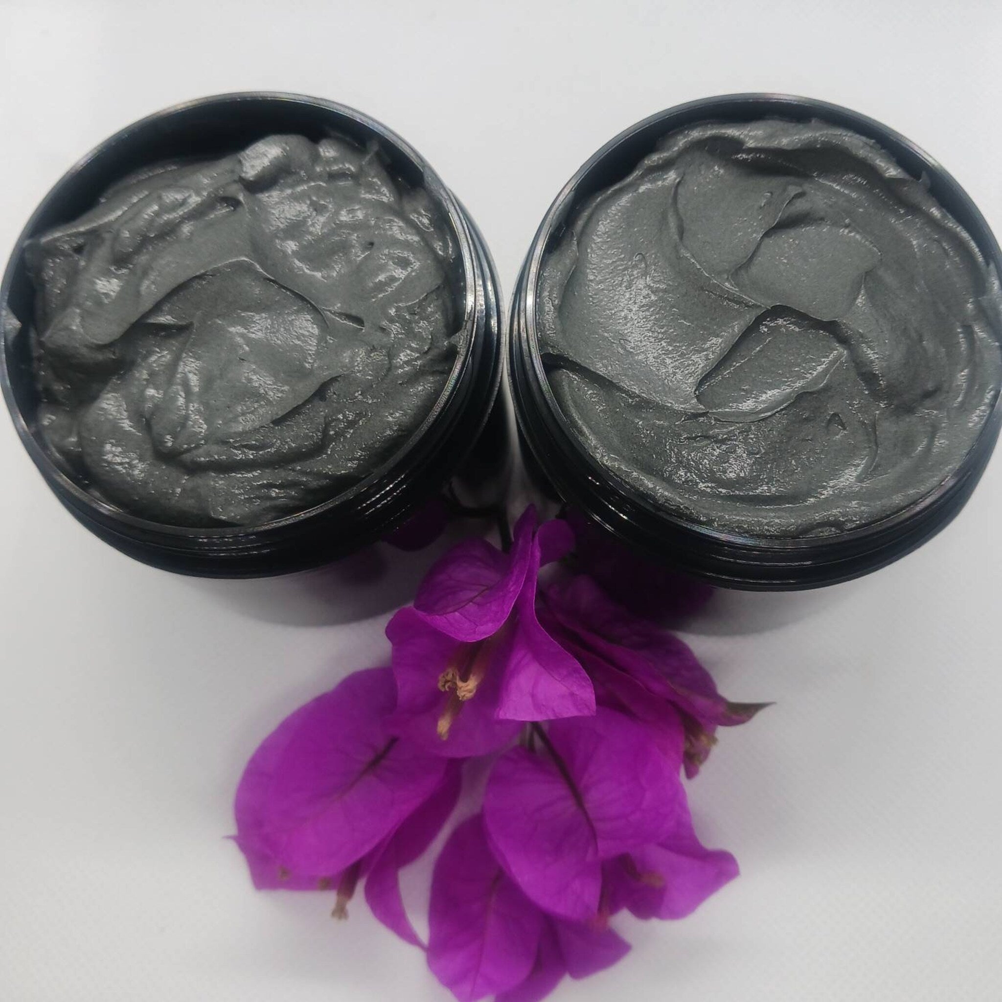 Close-up of black charcoal and golden turmeric face mask in a jar with wooden spatula on marble surface