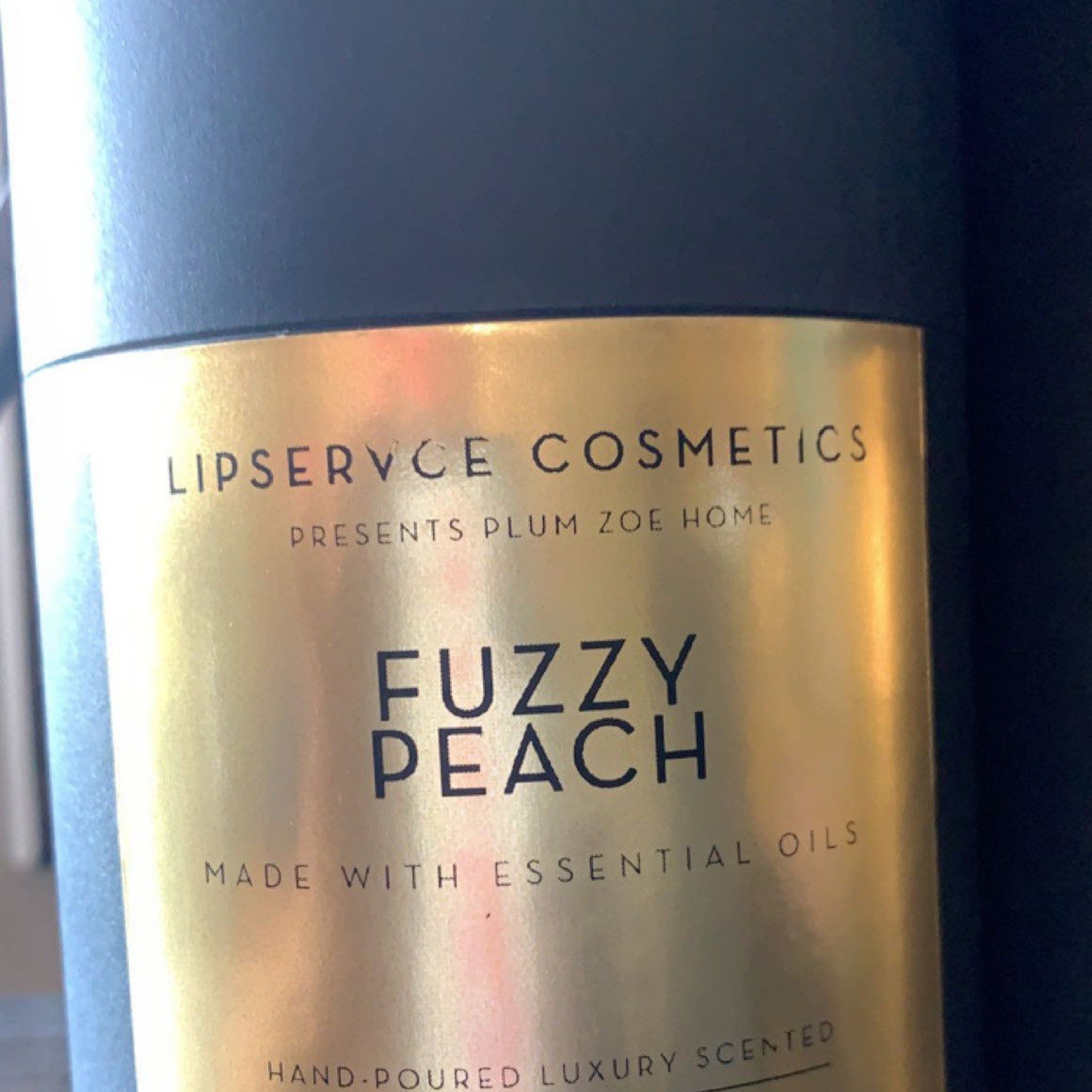 Fuzzy Peach candle with gold label, black background, and brand Lipservce Cosmetics text visible