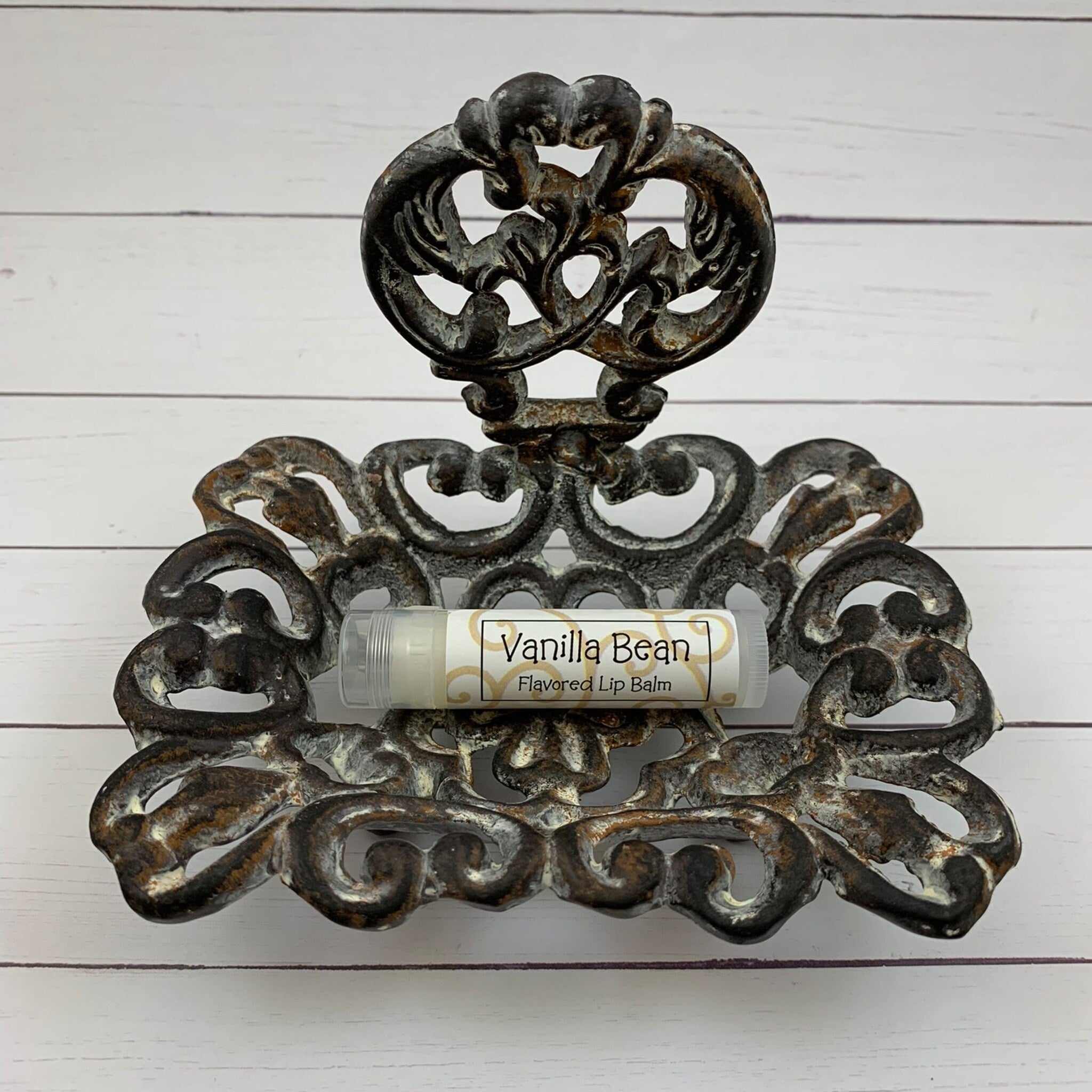 Lip balm tube with "Vanilla Bean" label in ornate metal holder, on white wood surface