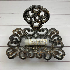 Lip balm tube with "Vanilla Bean" label in ornate metal holder, on white wood surface