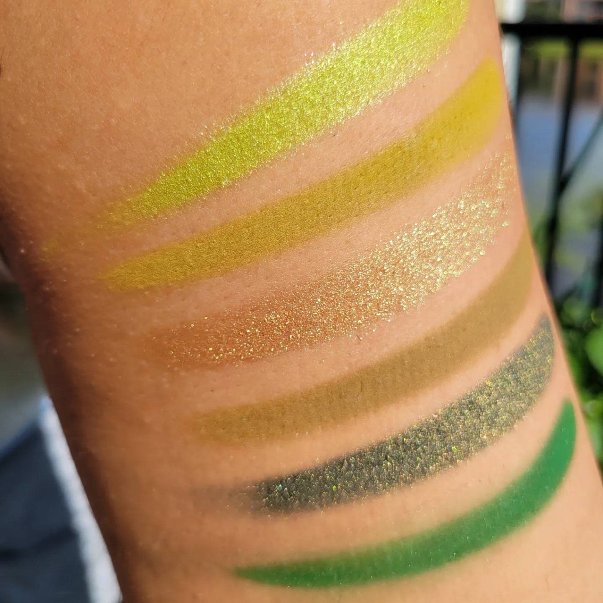 Top-down view of six green eyeshadow pans in earthy herb shades arranged in sleek black compact