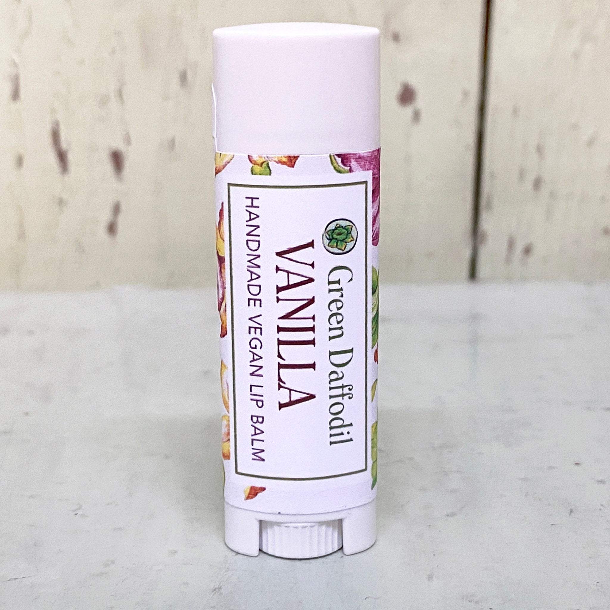 Lip balm tube with white and floral label, "Green Daffodil" and "Vanilla" text visible
