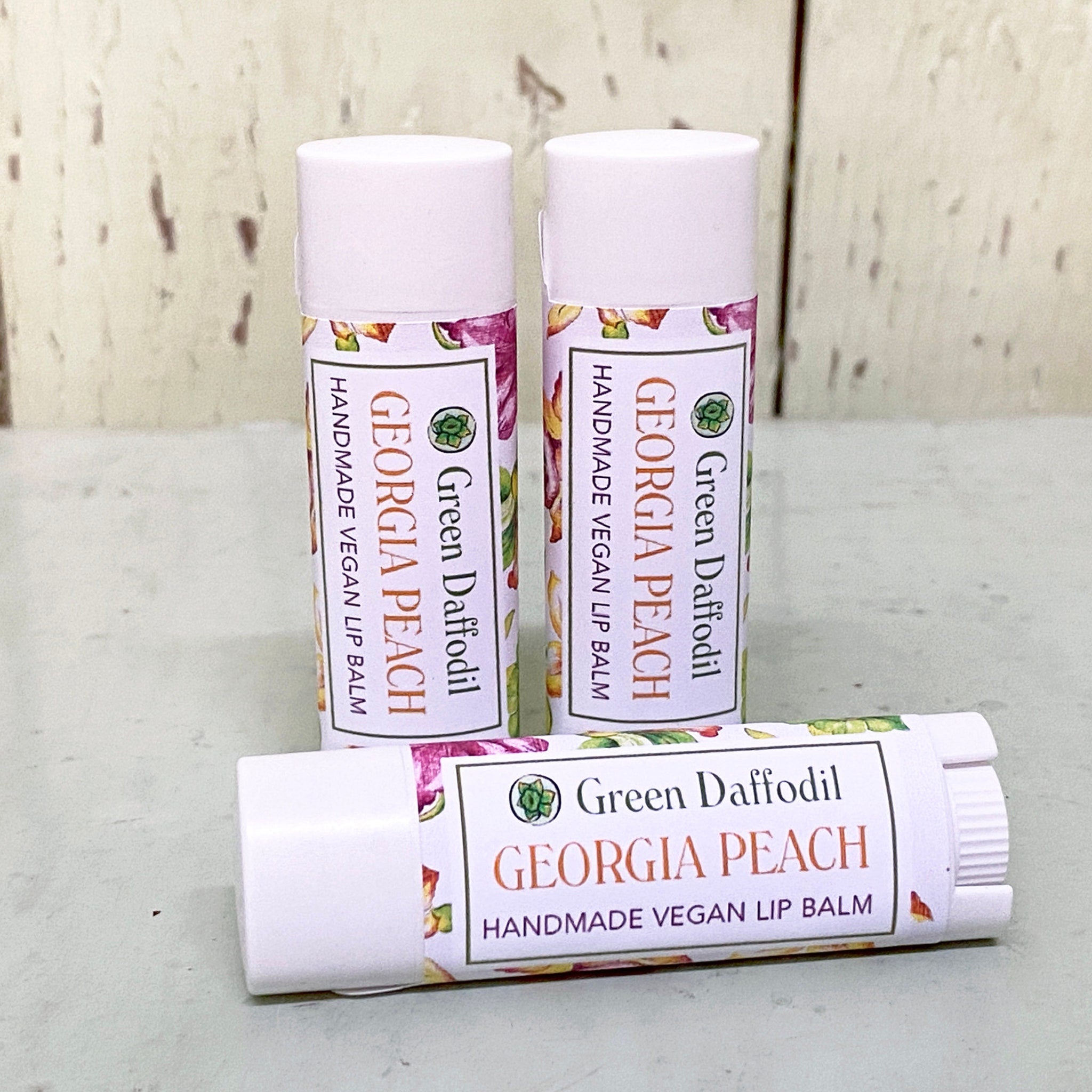 Lip balm tubes with white caps, floral pattern, and Green Daffodil Georgia Peach label