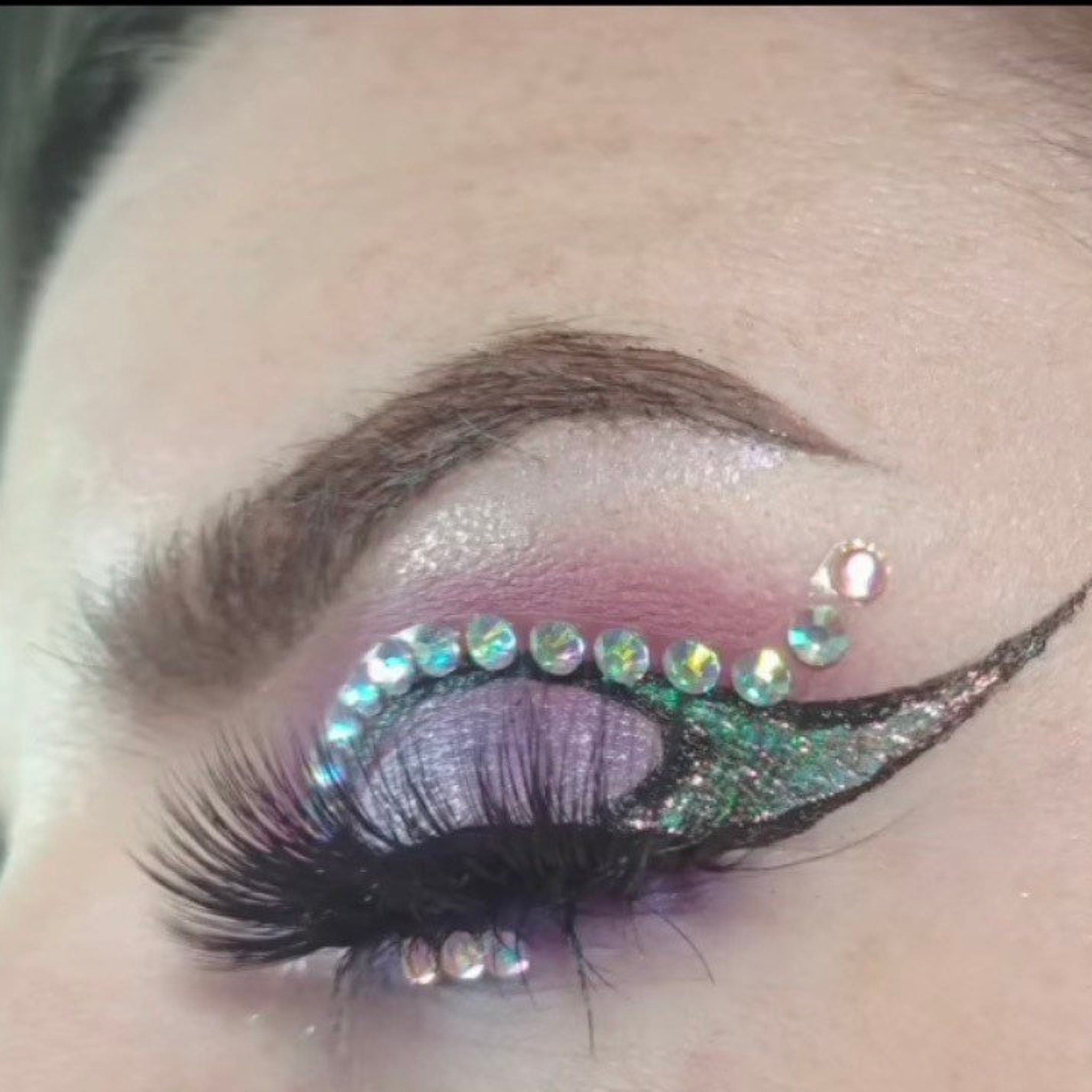 Eye makeup with purple, green, and silver glitter, and iridescent rhinestones on eyelid