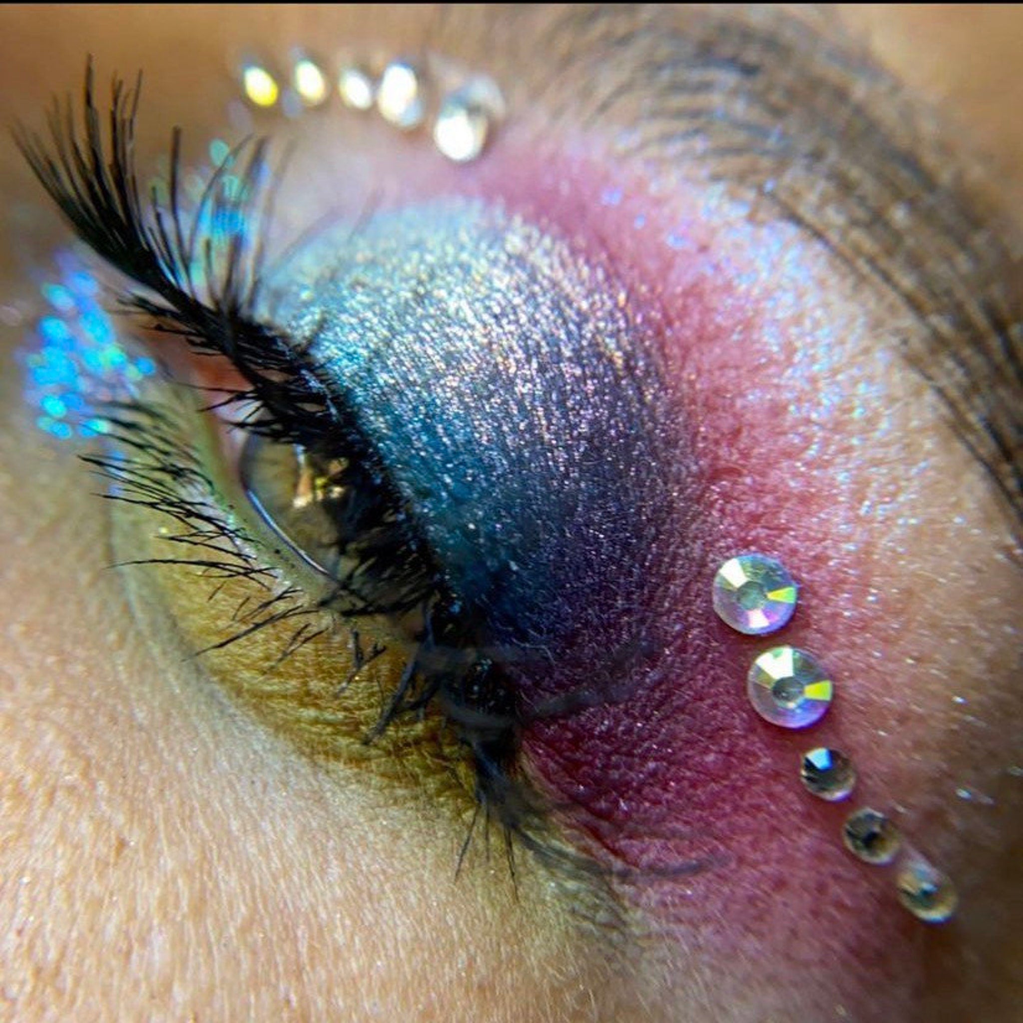 Eye makeup with blue, purple, and pink eyeshadow, black mascara, and clear rhinestones on the eyelid