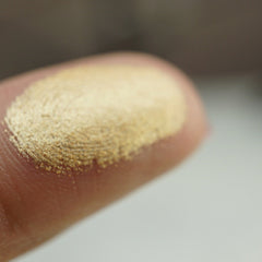 Side view of light gold shimmer pressed pigment in round pan showing metallic finish