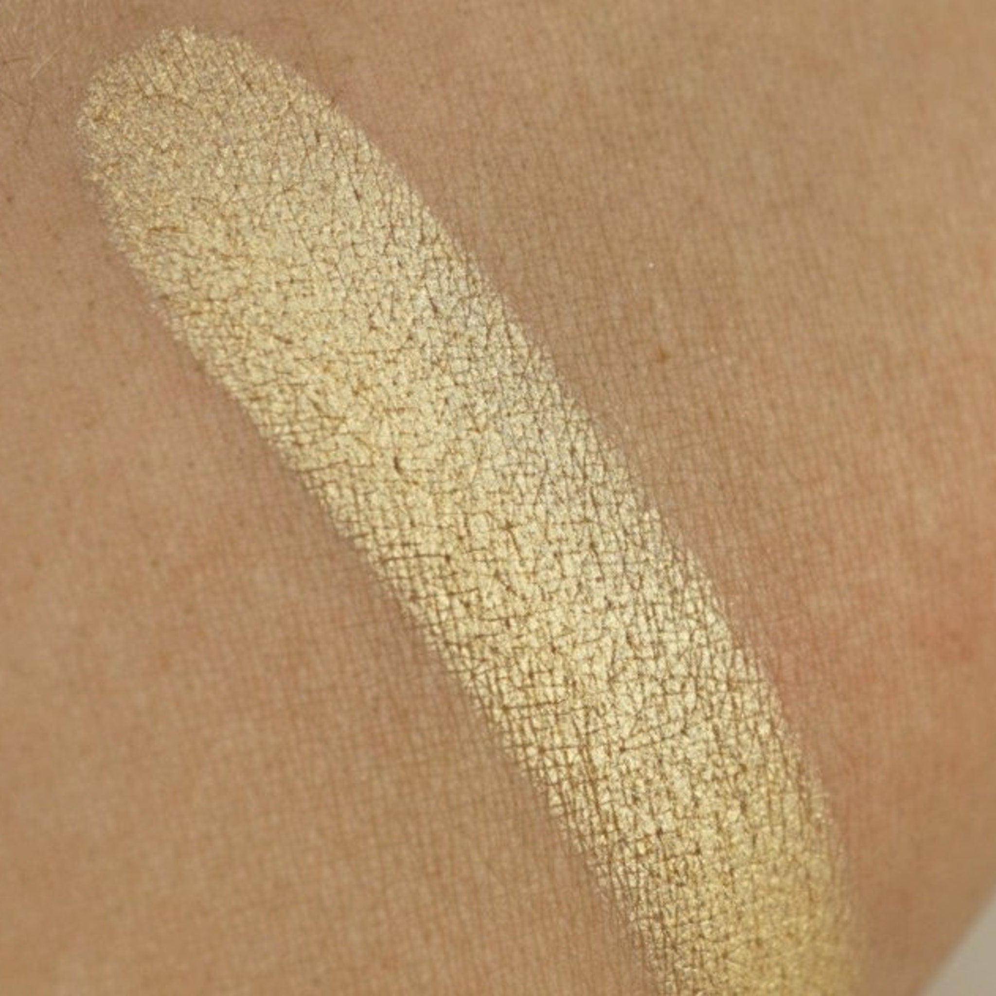 Close-up of light gold shimmer pressed pigment with intense metallic finish in round pan